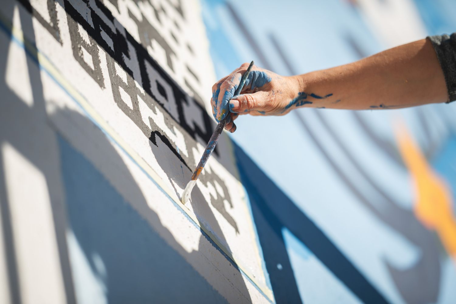 Close-up of a hand painting a wall with a roller in bright daylight.