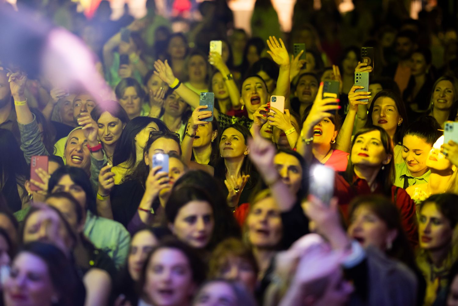 Energetic concert crowd cheering and raising hands under stage lights at a night festival.