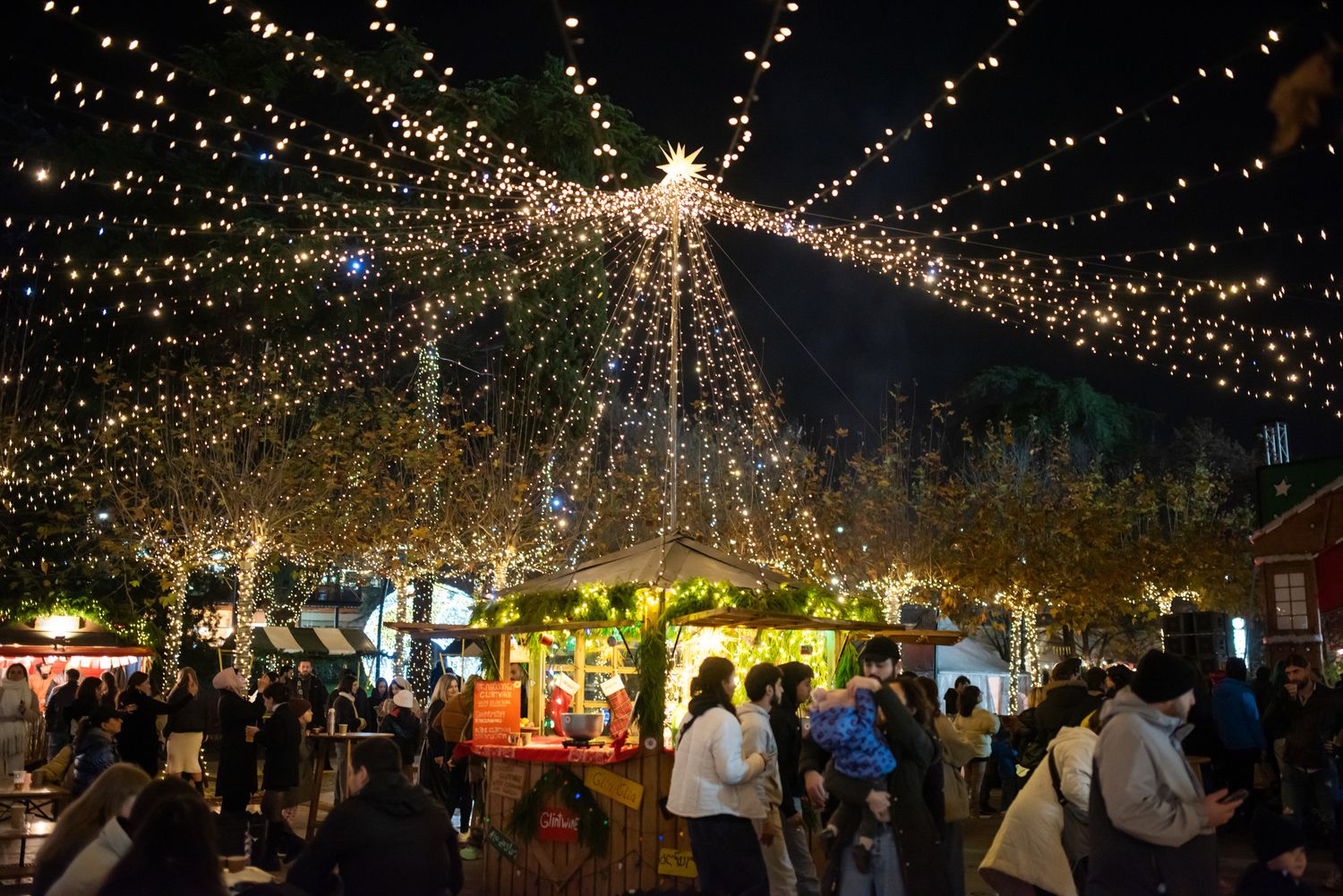 Evening market illuminated with festive string lights and a crowd enjoying the night.