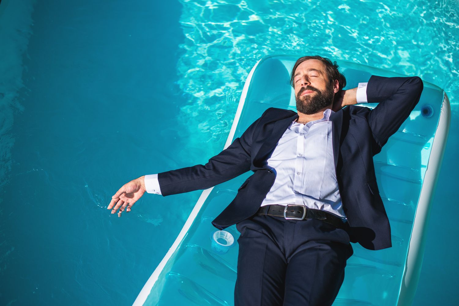 Smiling man in suit relaxing underwater — surreal business portrait in a blue pool.