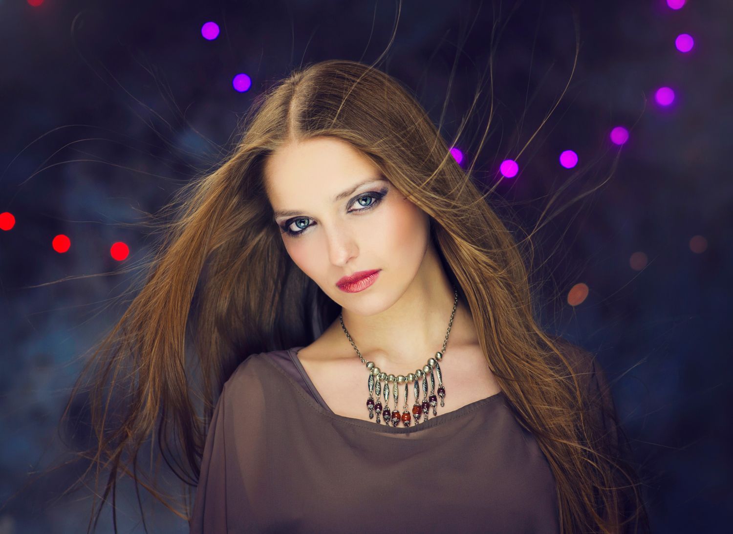 Glamorous studio-style portrait of a woman with long hair and violet lighting in the background.