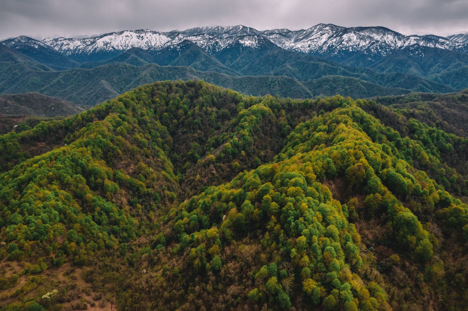 Drone view of lush green mountain ranges under a cloudy sky.
