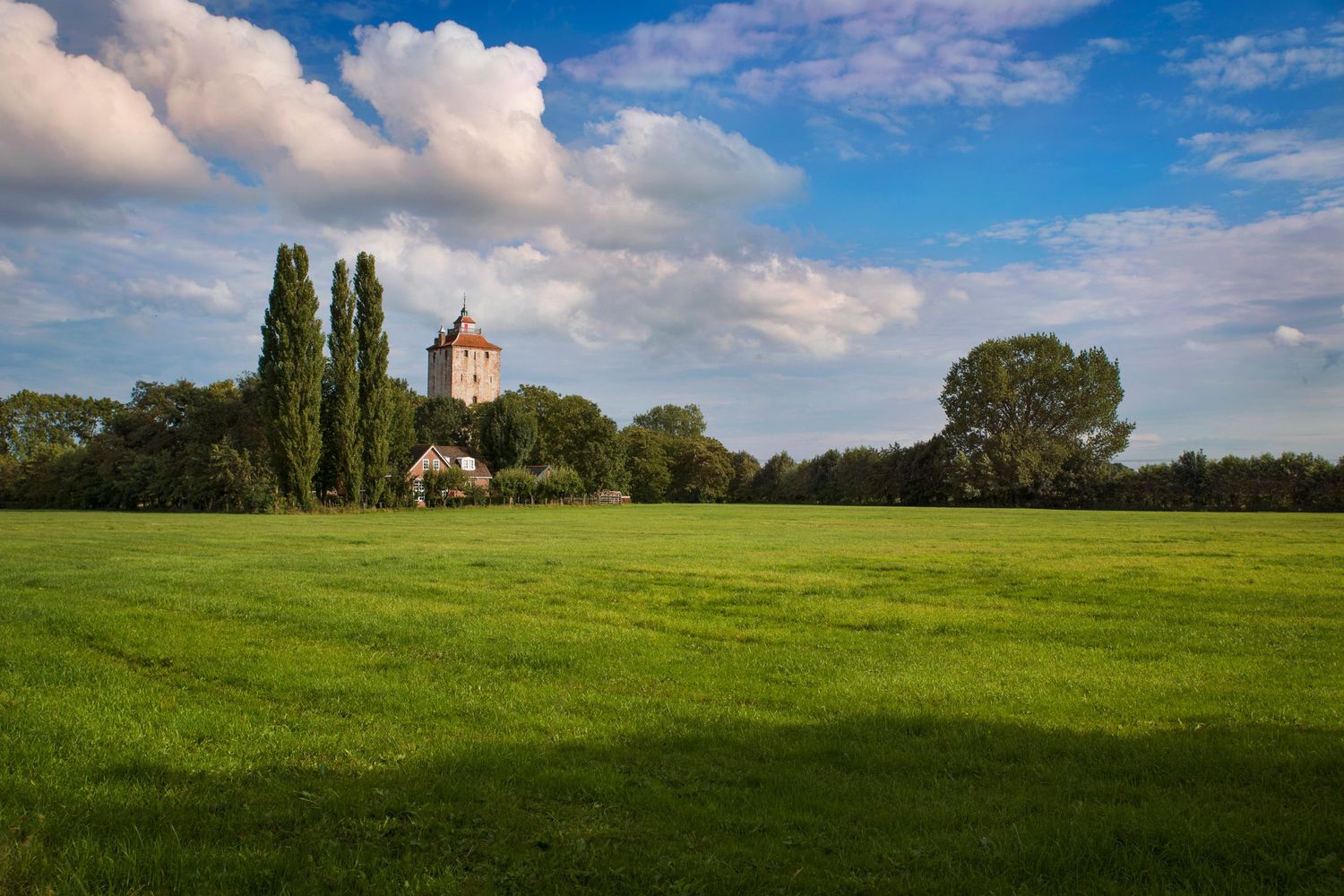 Scenic rural landscape with a small church surrounded by trees, under a blue sky with scattered clouds.