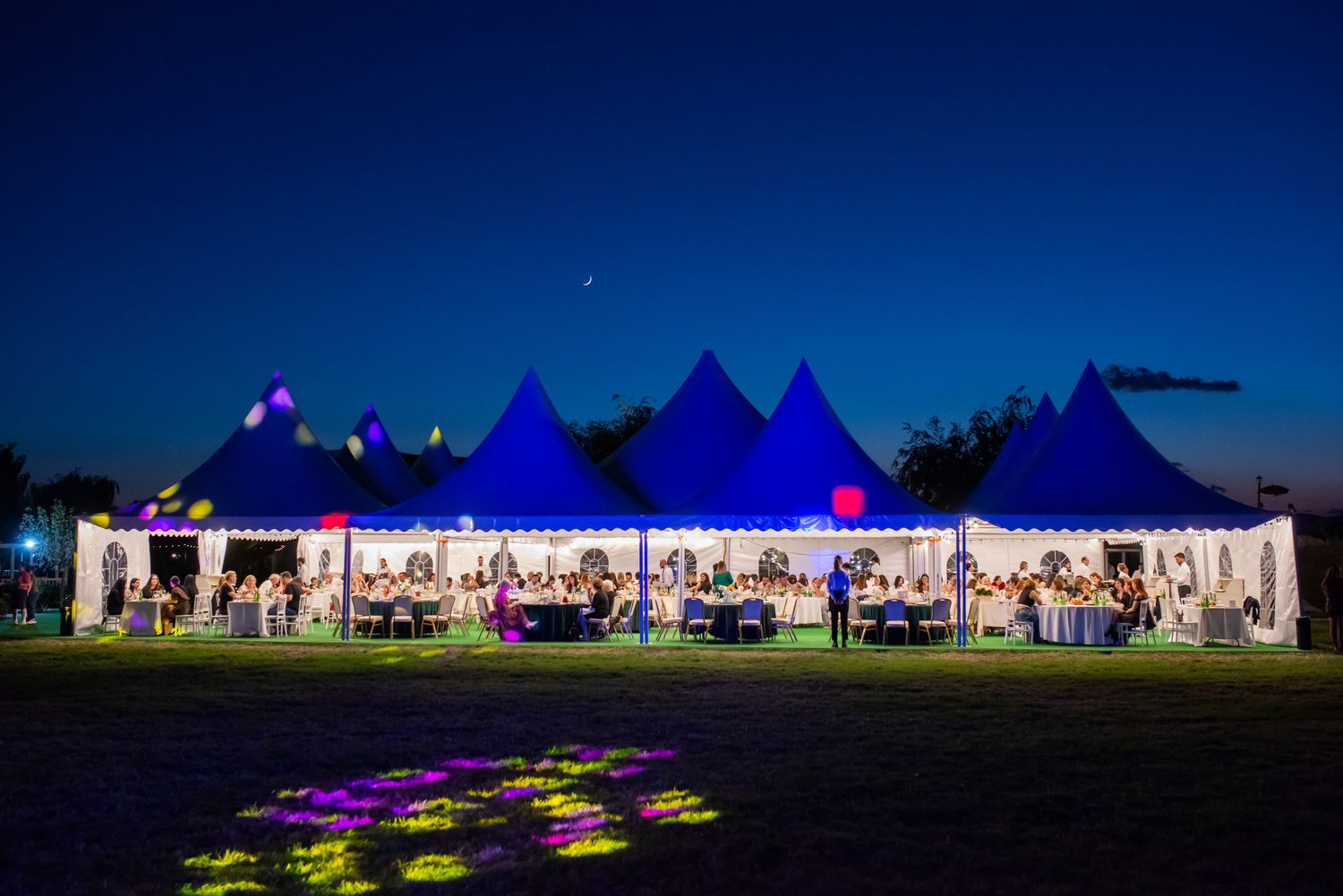 Outdoor event tent illuminated at night with blue lighting and decorative projections on the ground.