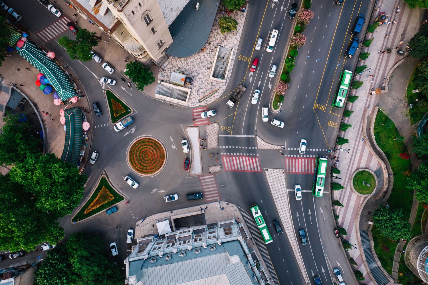 Top-down view of a roundabout surrounded by city streets and green patches in daylight.