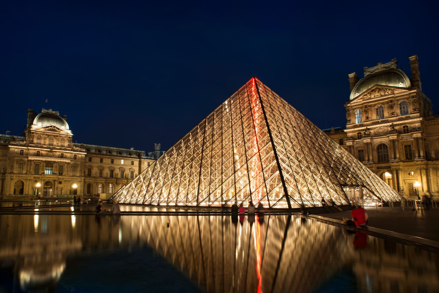 The Louvre Pyramid illuminated at night — iconic Paris architecture blending modern and classical styles.
