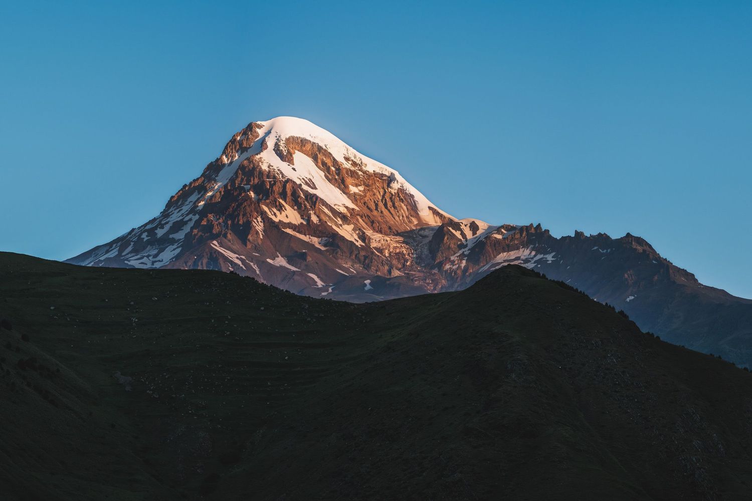 Snow-capped Mount Kazbegi, glowing at sunrise — iconic Georgian peak with a dramatic backdrop.