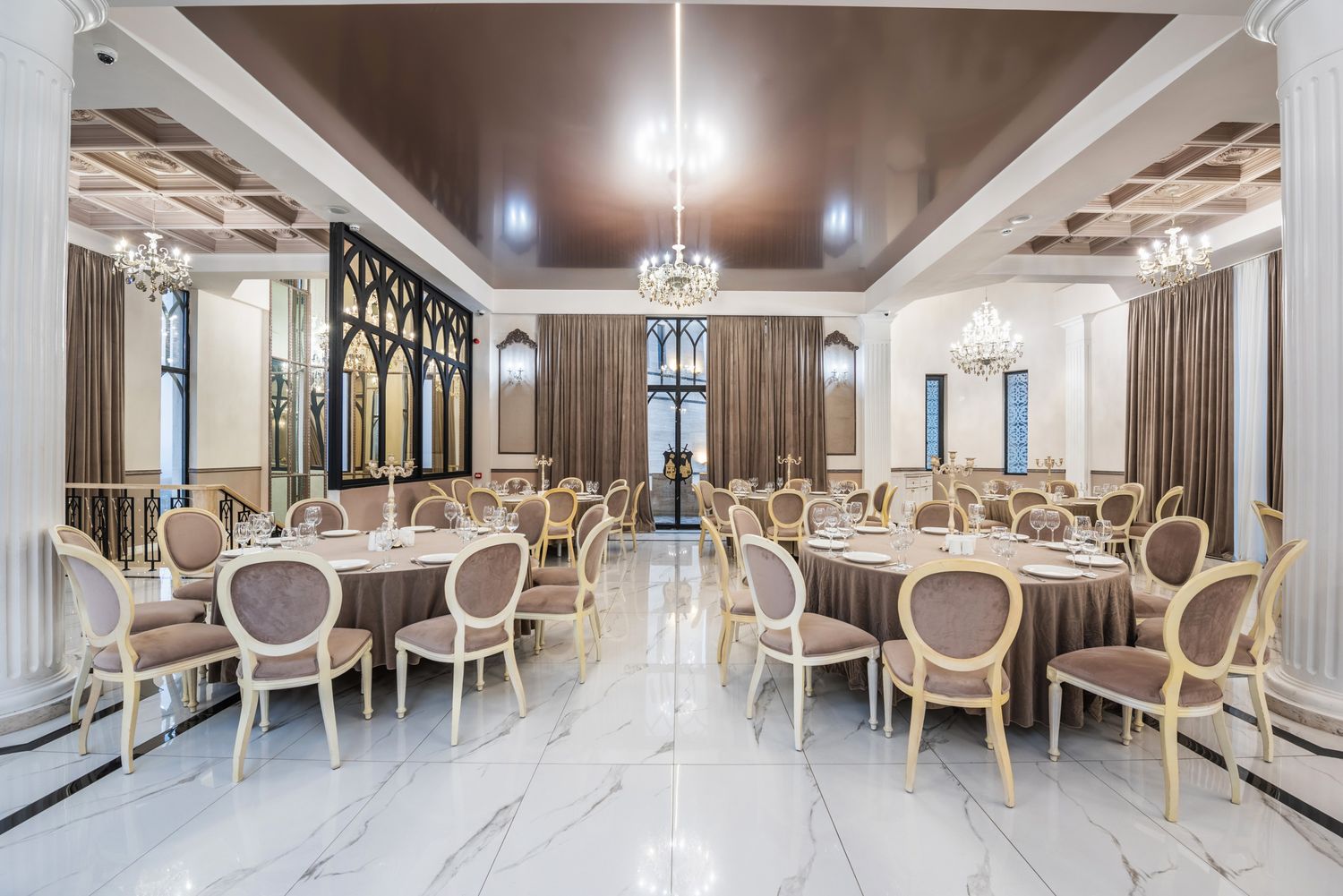 Elegant dining hall with cream-colored chairs and chandeliers, featuring classical molding and a refined design.