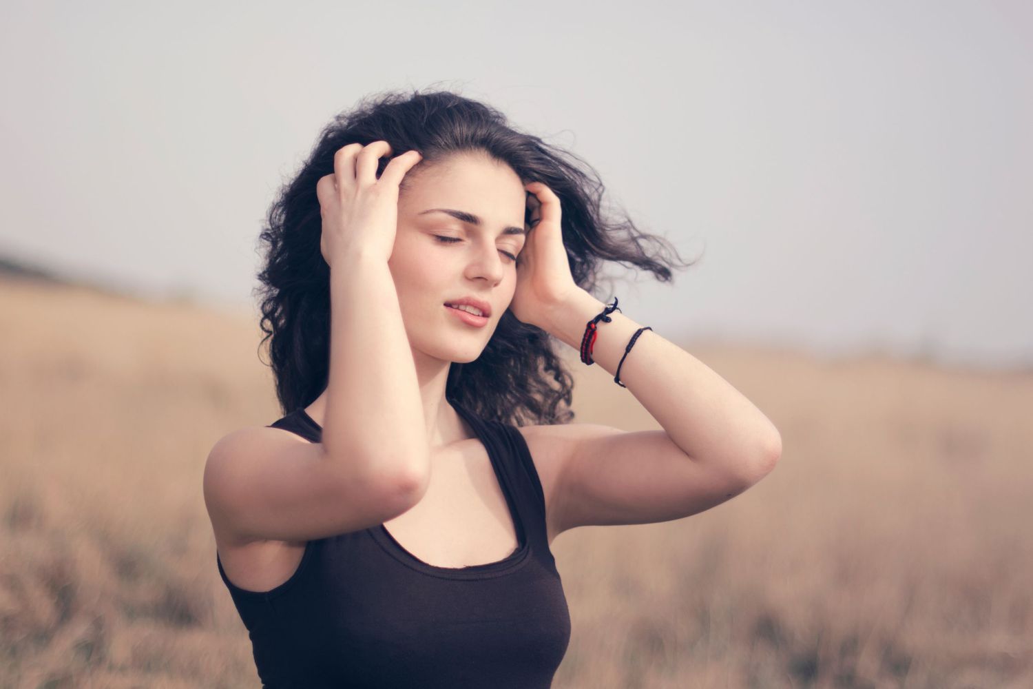 Portrait of a joyful woman in a black dress posing outdoors in a sunlit field—captures natural beauty and carefree moments.