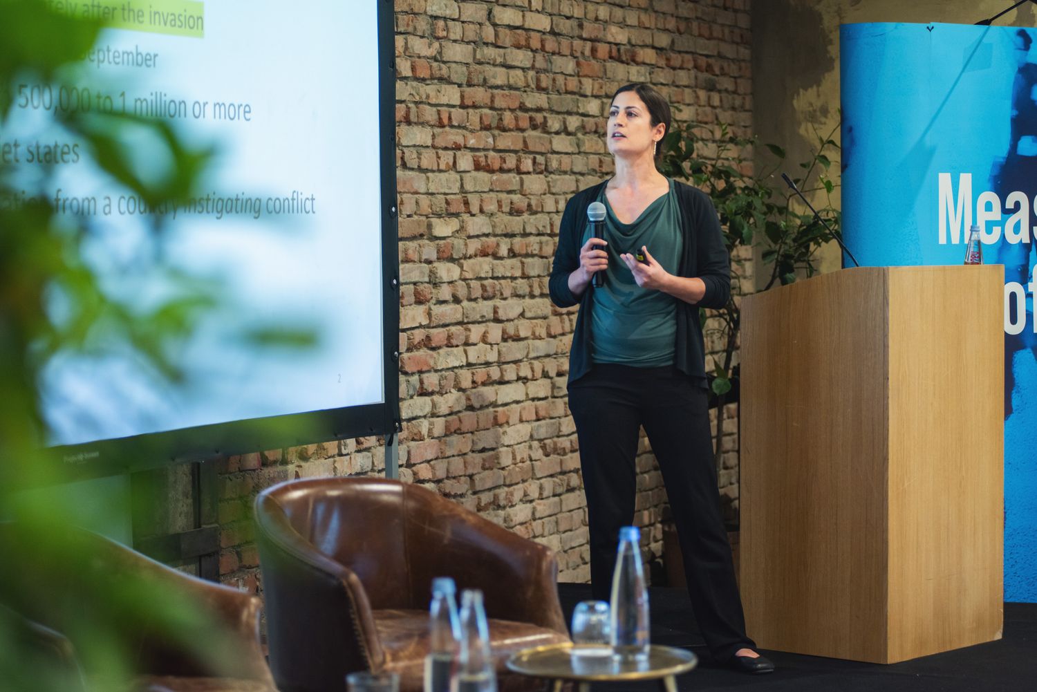 Woman delivering a presentation at a branded event, standing beside a podium and a conference banner.