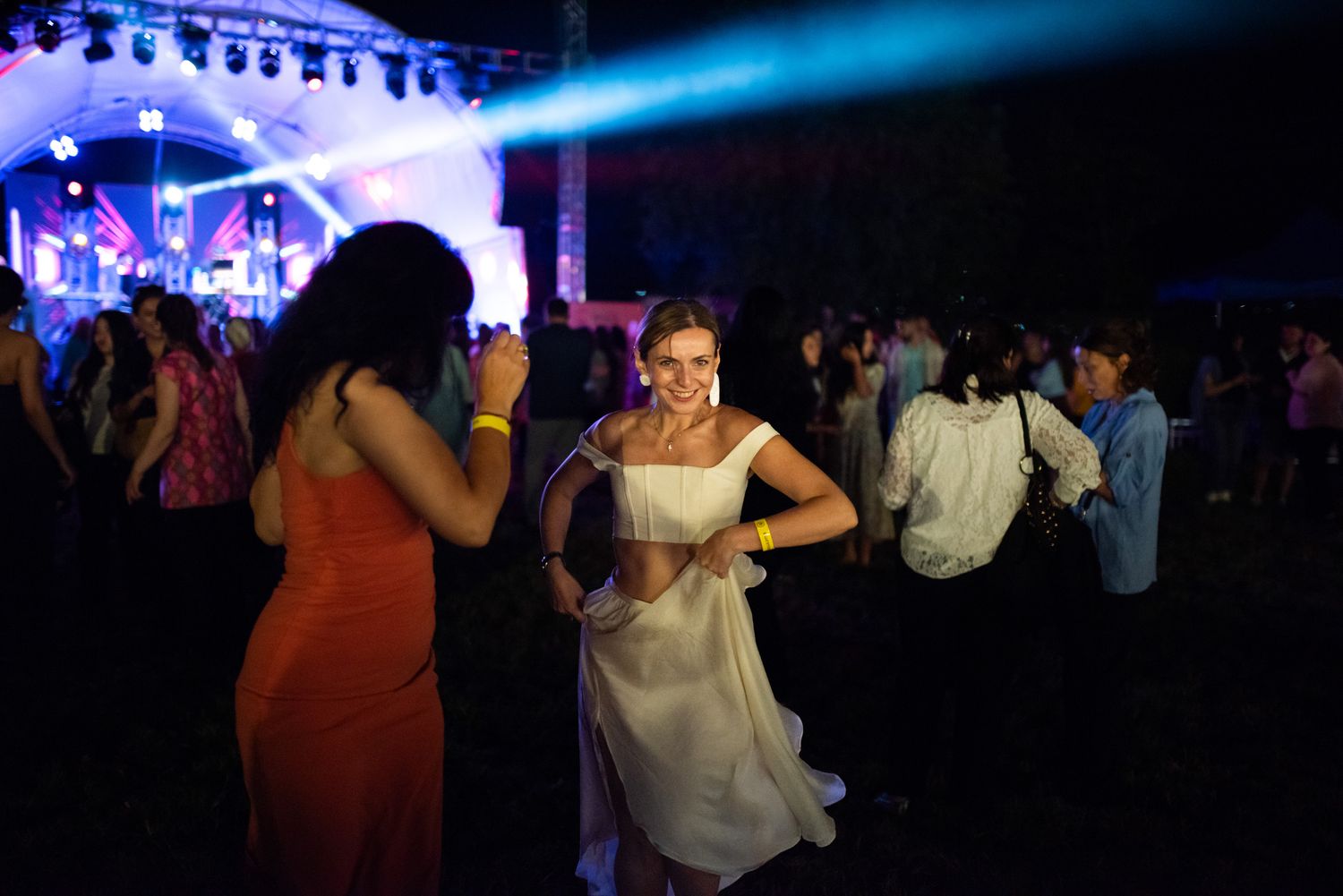 Couples dancing joyfully at an open-air night event, vibrant lighting in the background.
