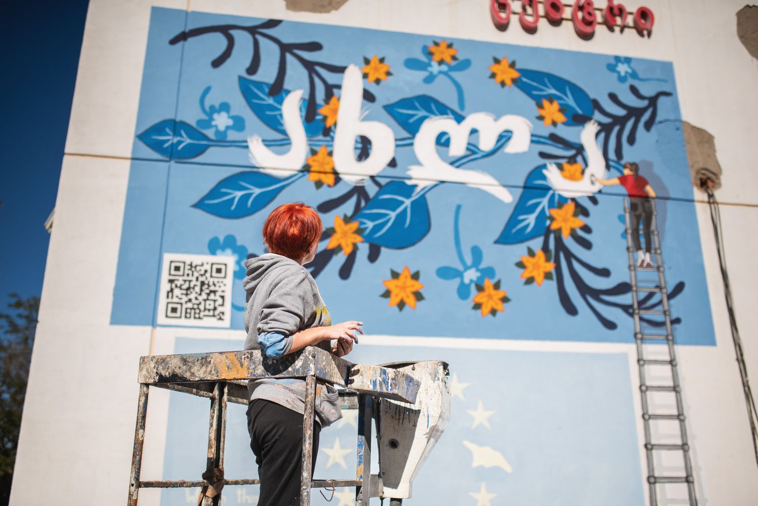 Colorful building wall art with the Georgian word “თიბისი” and characters playing in the sky.