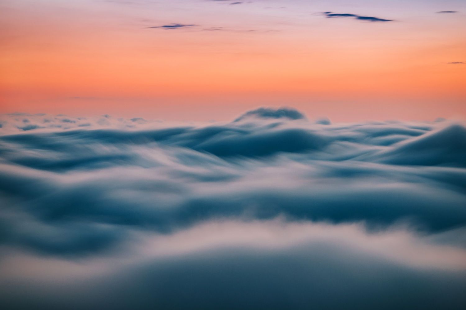 Sunrise above the clouds with warm orange tones and mist rolling over hilltops — aerial-style perspective.
