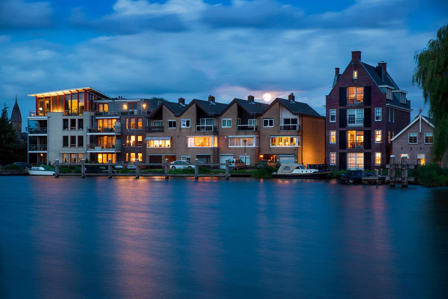 Modern waterfront homes with lights glowing at blue hour — peaceful evening over calm water.