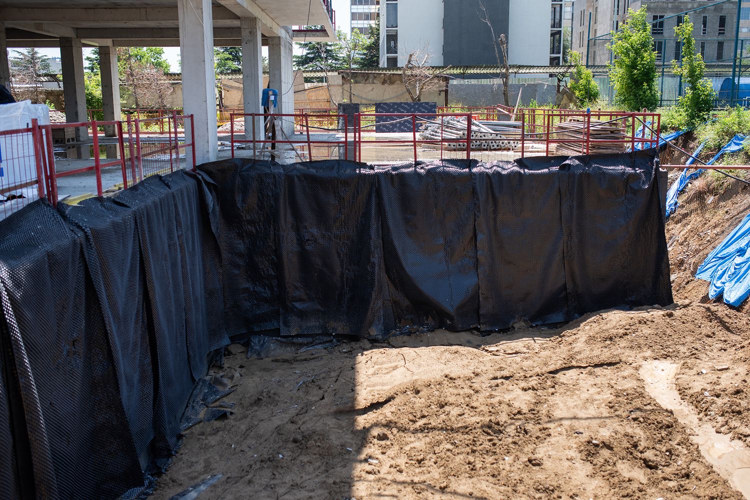 Excavated construction foundation covered with black waterproofing membranes.