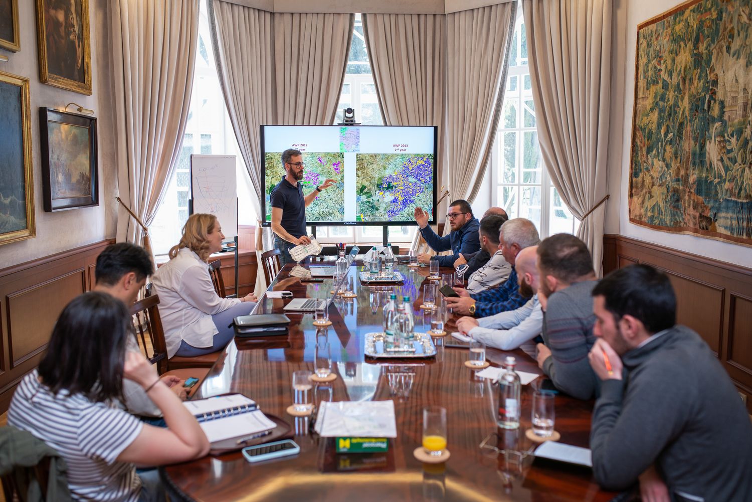 Formal meeting with multiple participants gathered around a long table in an elegant room.