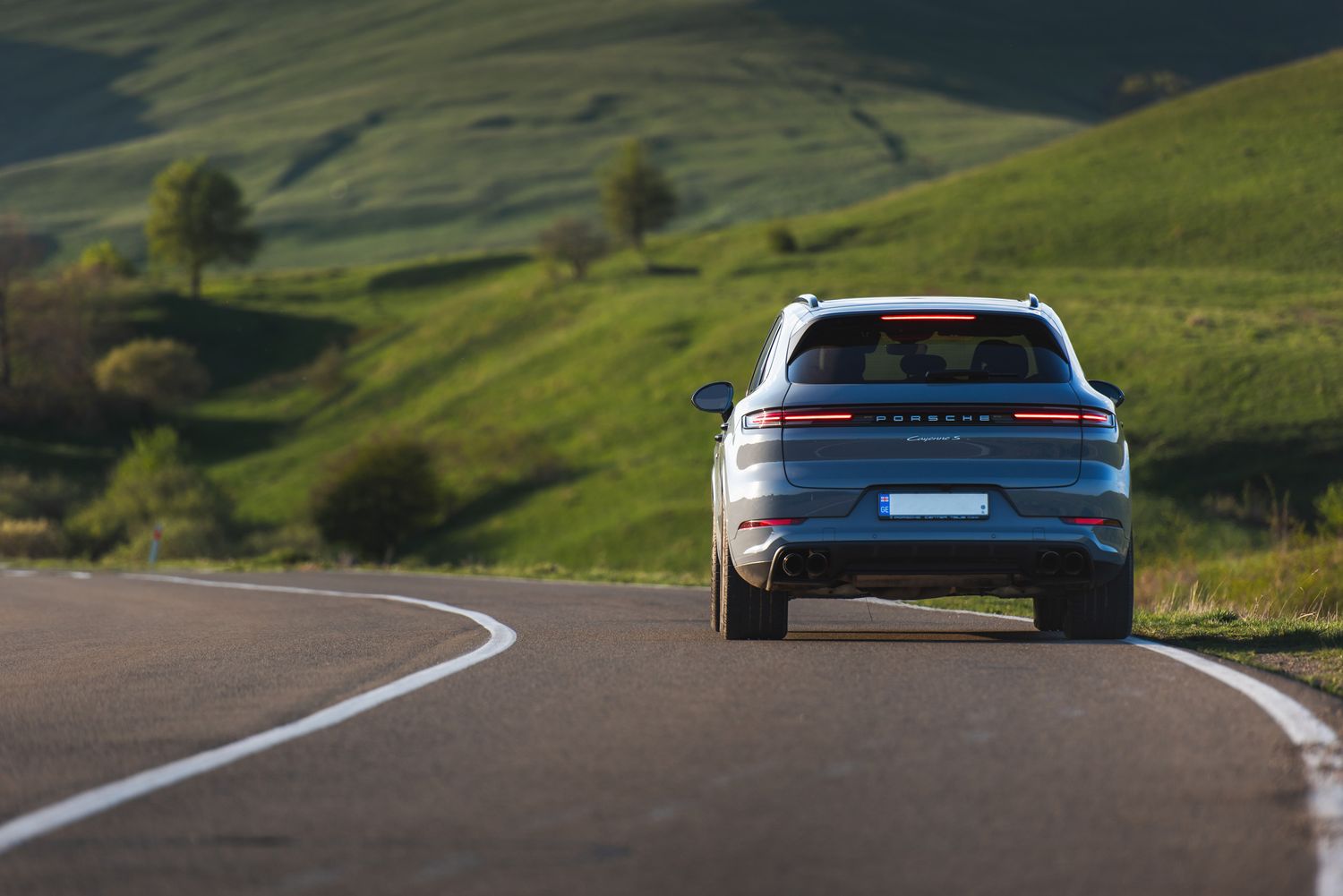 Rear view of a white car cruising through green hills — open road freedom concept.