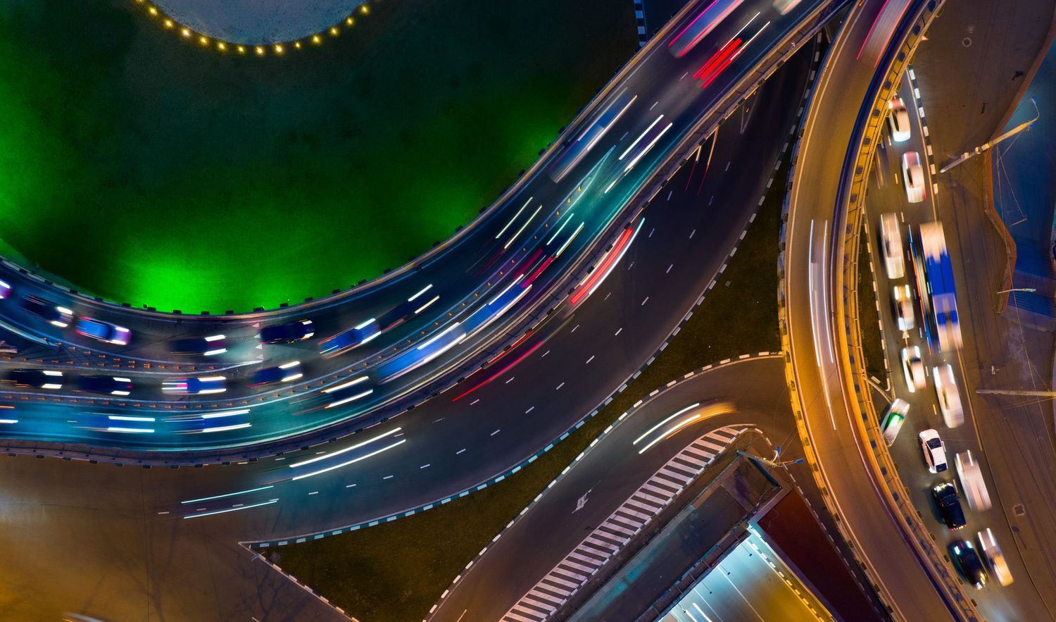 Colorful aerial view of multilane highway interchange at night — light trails and traffic flow.