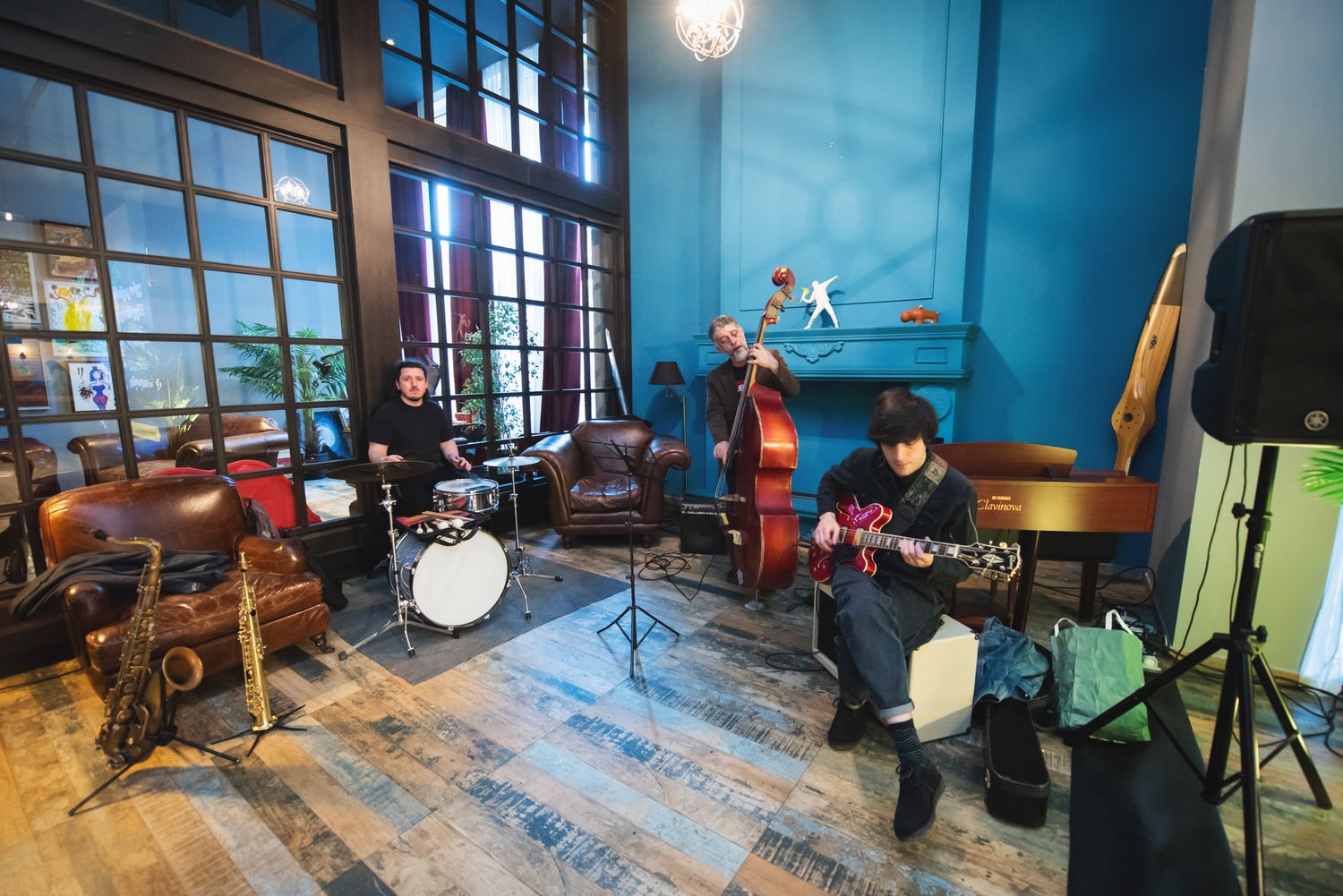 Band rehearsing in a colorful, artsy studio space with musical instruments and sunlight through windows.