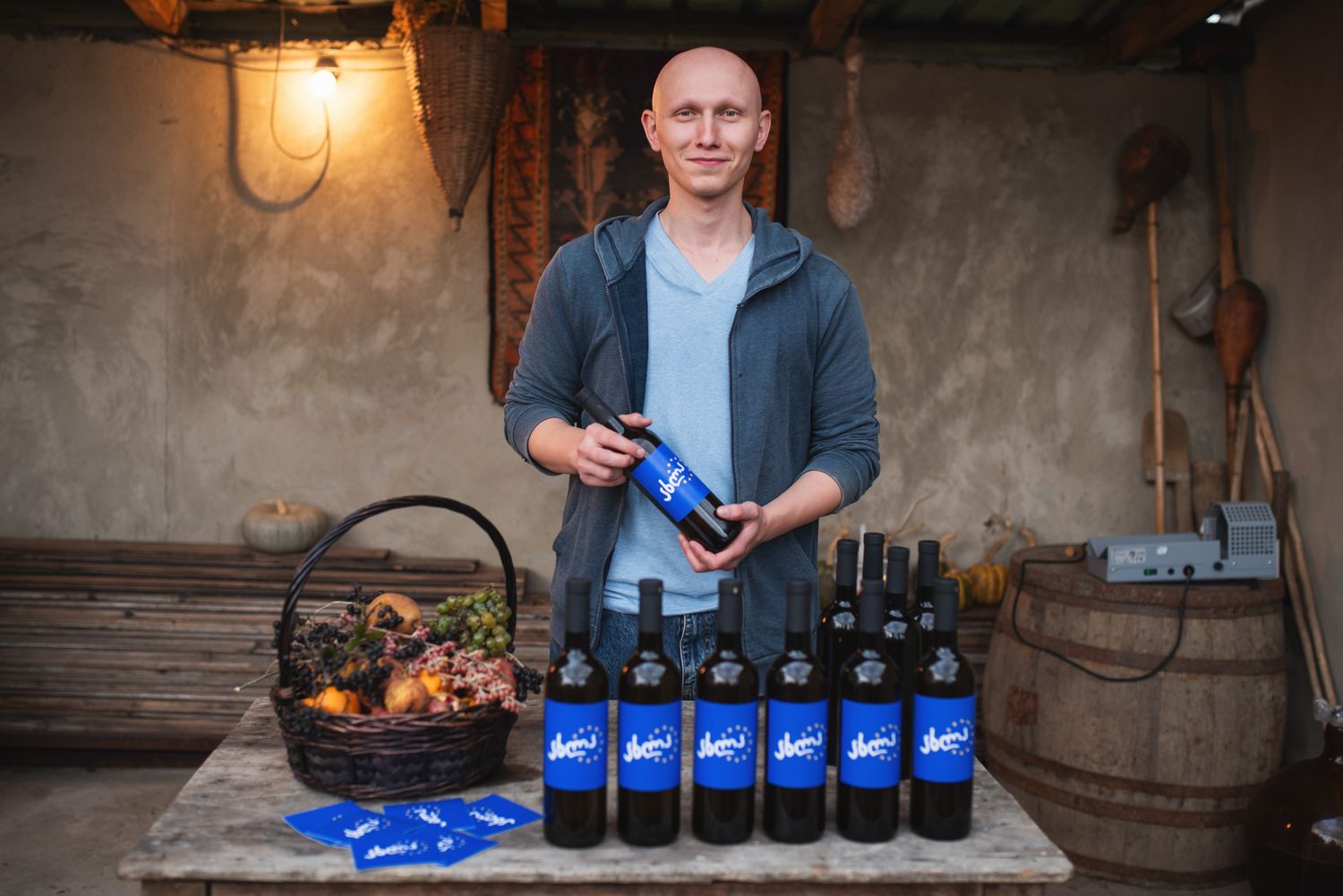 Man presenting locally made wine bottles and artisanal products on a rustic table.