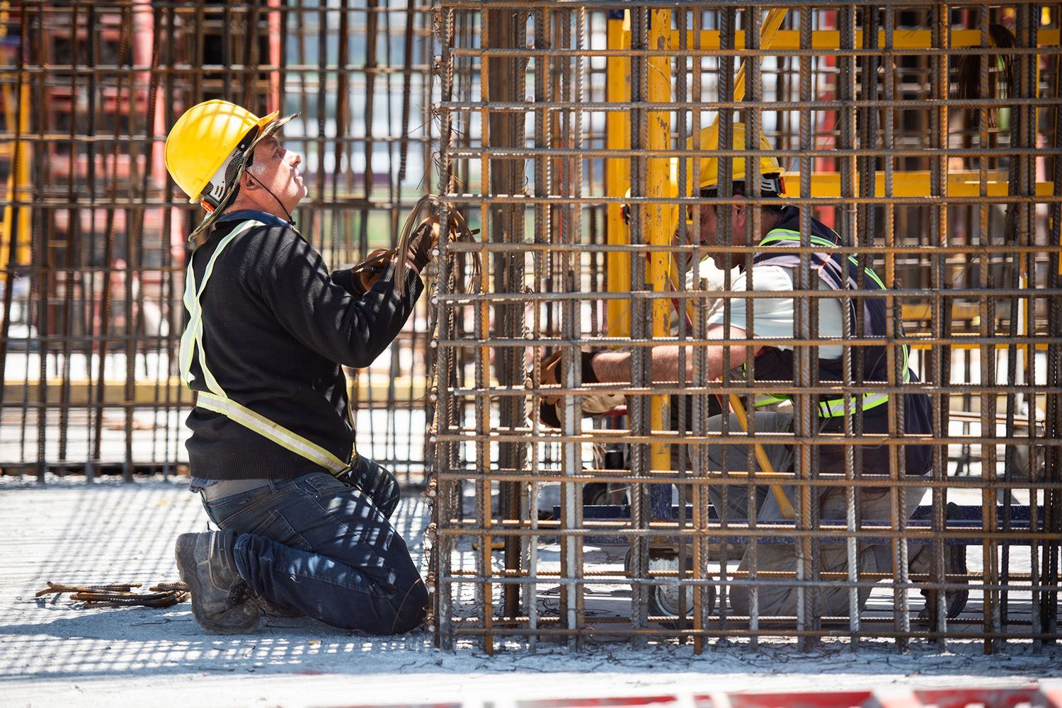 Engineer or foreman using a walkie-talkie amid dense steel reinforcements at a construction zone.