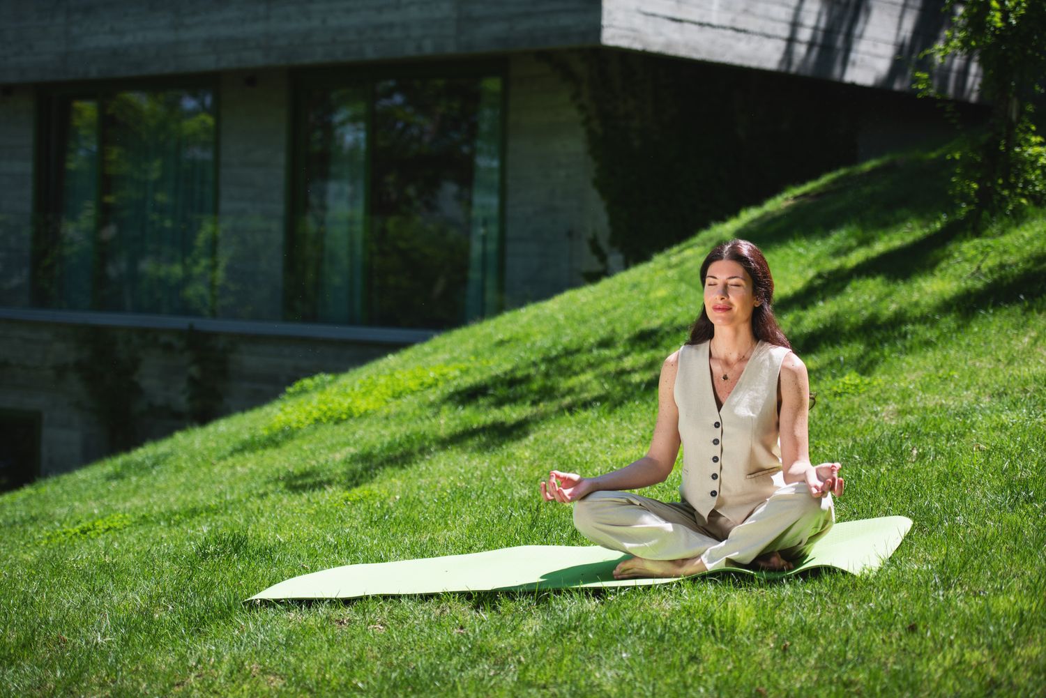 Woman practicing yoga on a green lawn — outdoor mindfulness session near modern building.
