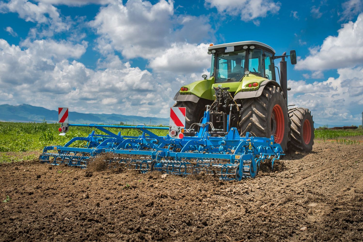 Tractor spreading fertilizer over a cultivated field on a sunny day.