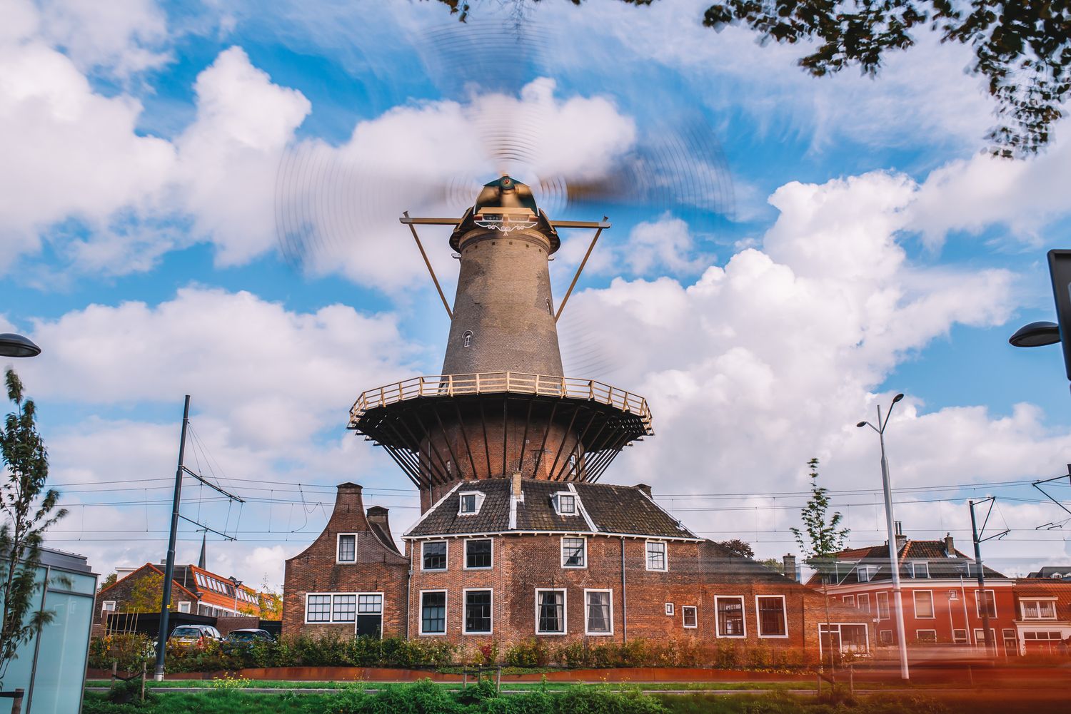 Traditional Dutch windmill with brick buildings under blue sky and scattered clouds — classic Netherlands scenery.
