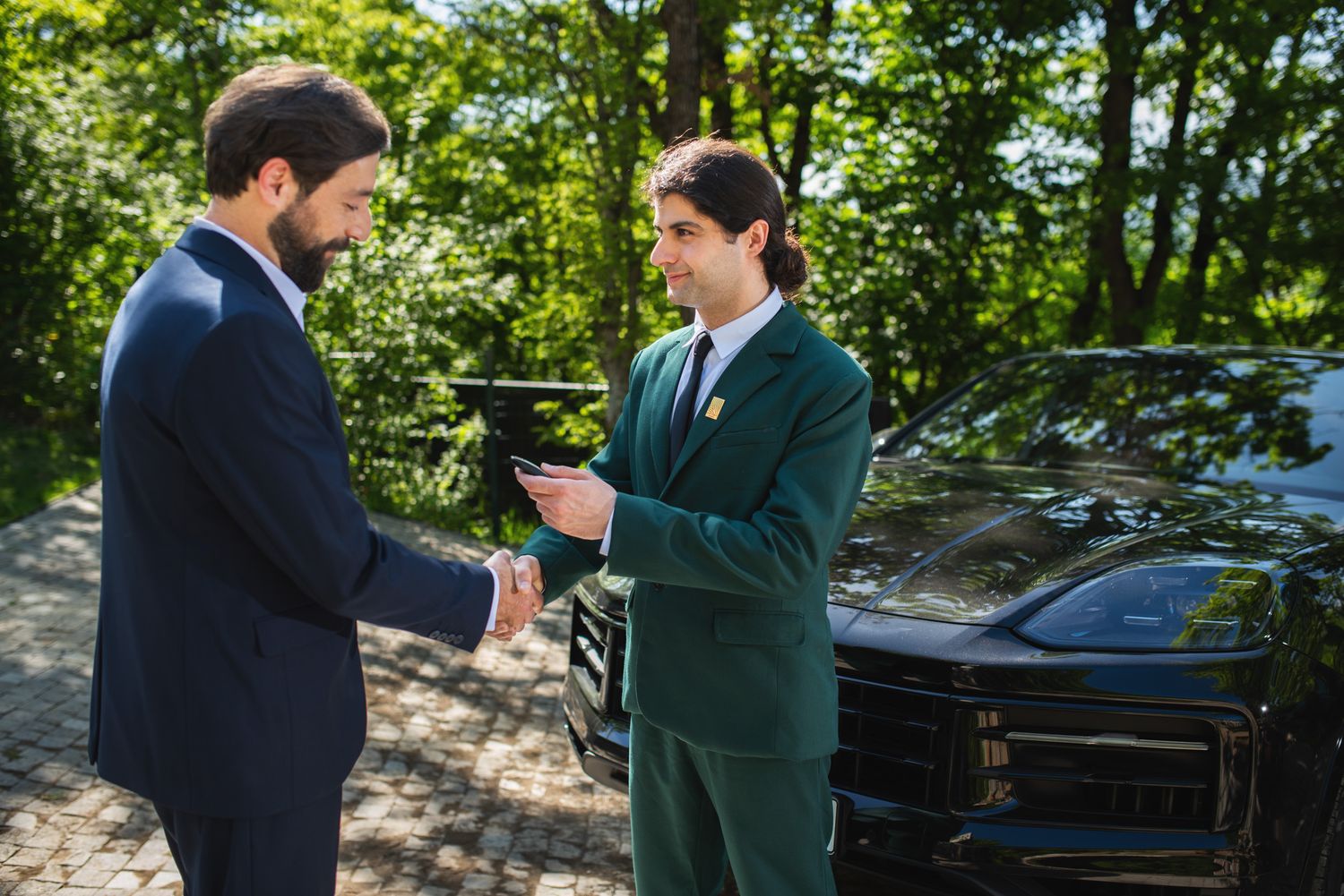 Handshake between two formally dressed men — professional agreement in a green urban setting.