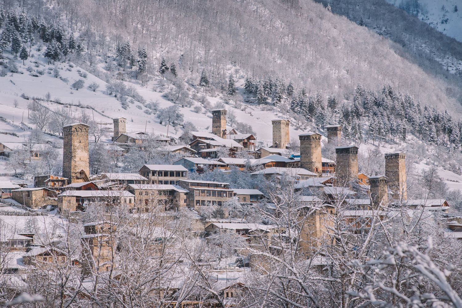 Winter aerial view of a Georgian town covered in snow, nestled among hills.