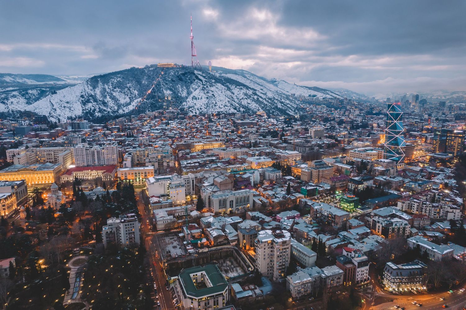 Winter cityscape of Tbilisi, with snow-covered rooftops and hills.