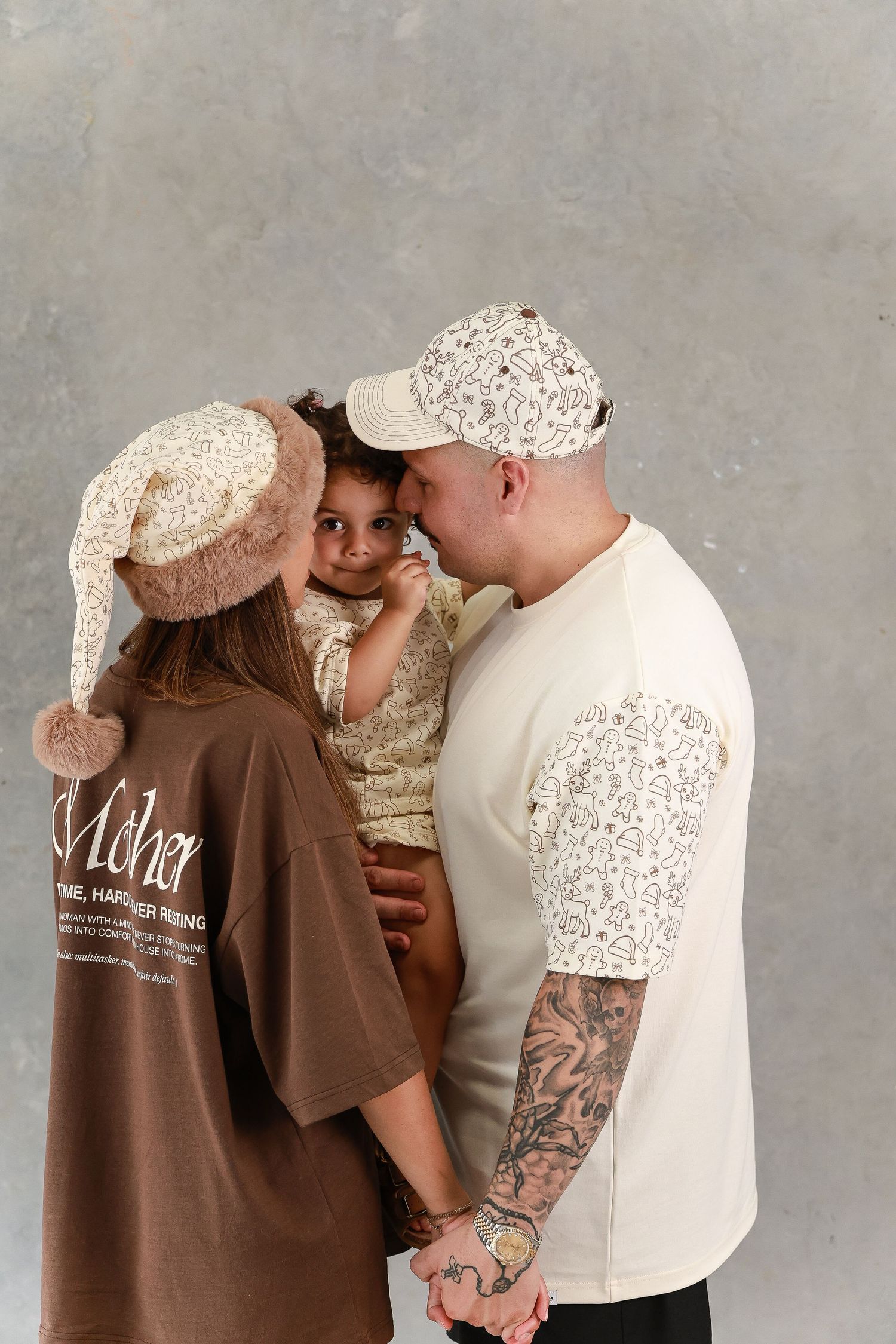 Family group wearing casual clothing and baseball caps sharing an intimate moment against grey background.