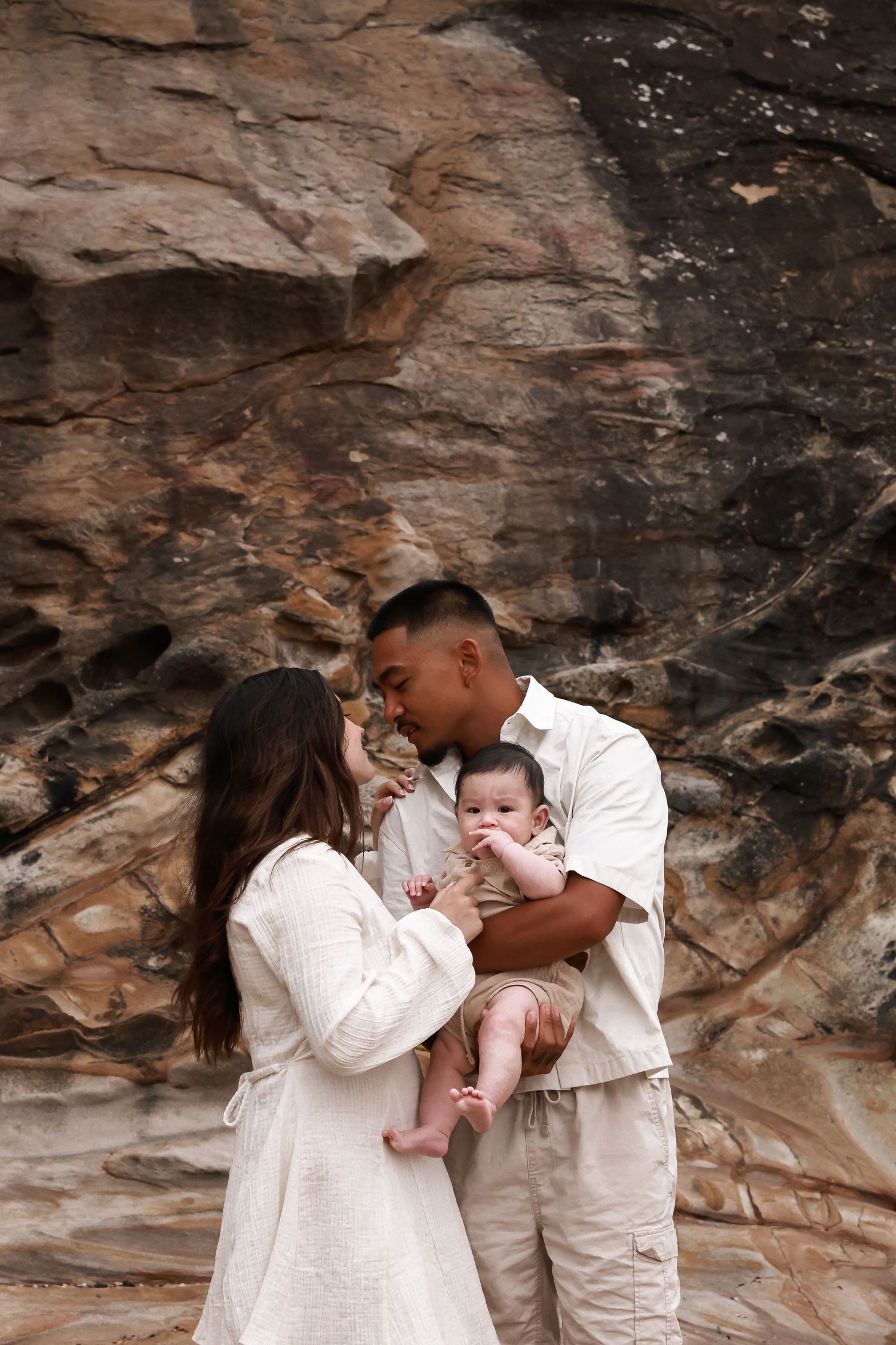 A family shares an intimate moment against weathered rock formations wearing matching white outfits.