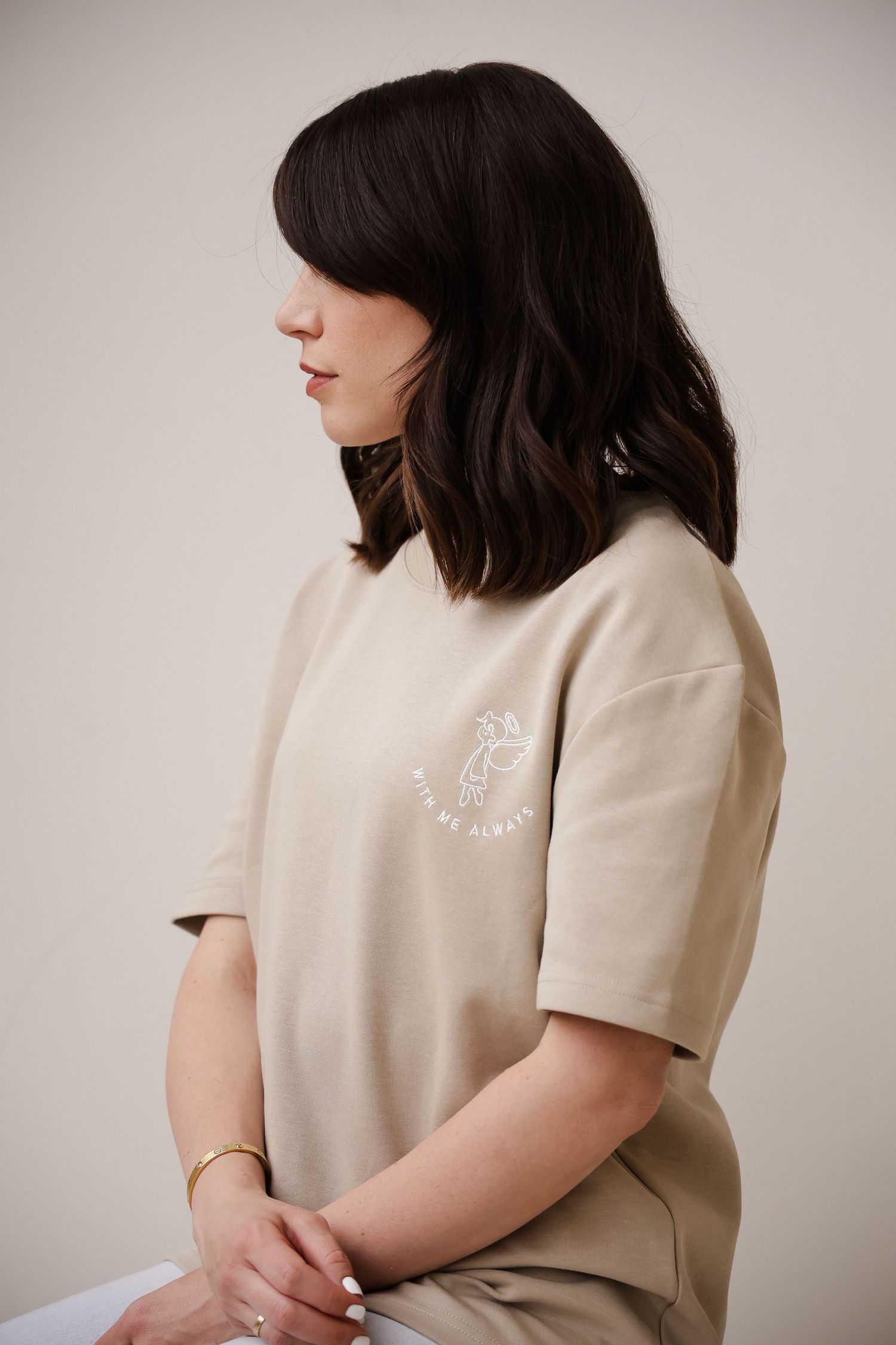 Side profile of someone wearing a beige short-sleeve top with minimal embroidered design.