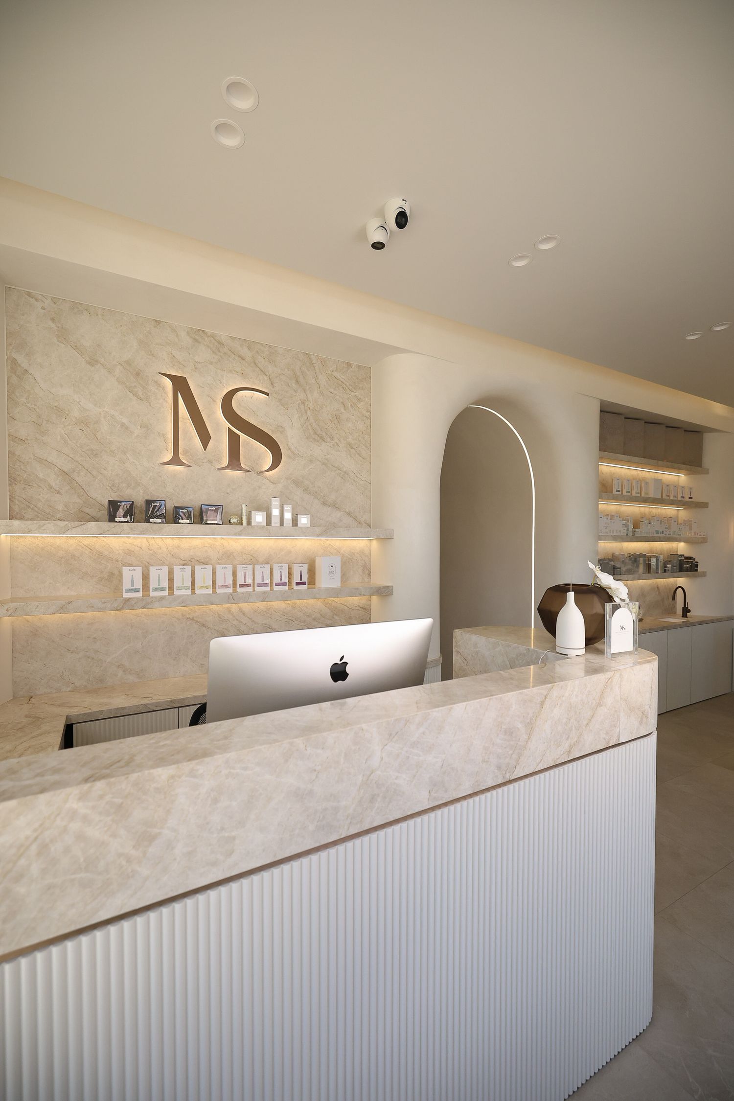Modern reception desk with illuminated MD logo, marble counter, and floating shelves.
