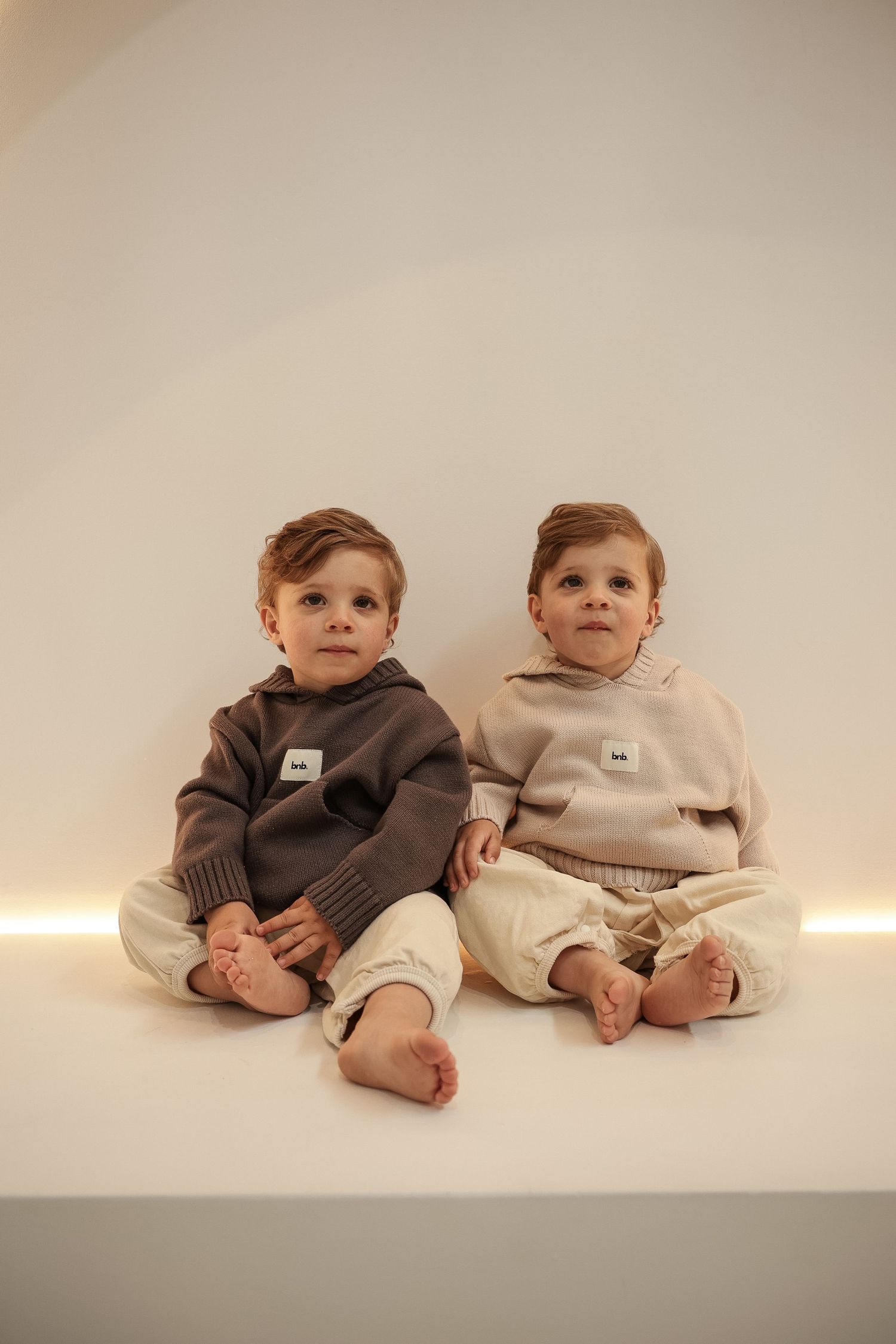 Two babies wearing coordinated loungewear sets sitting on white platform.