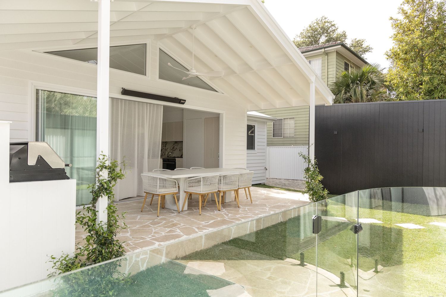 Contemporary outdoor dining area with glass barriers and pool view.