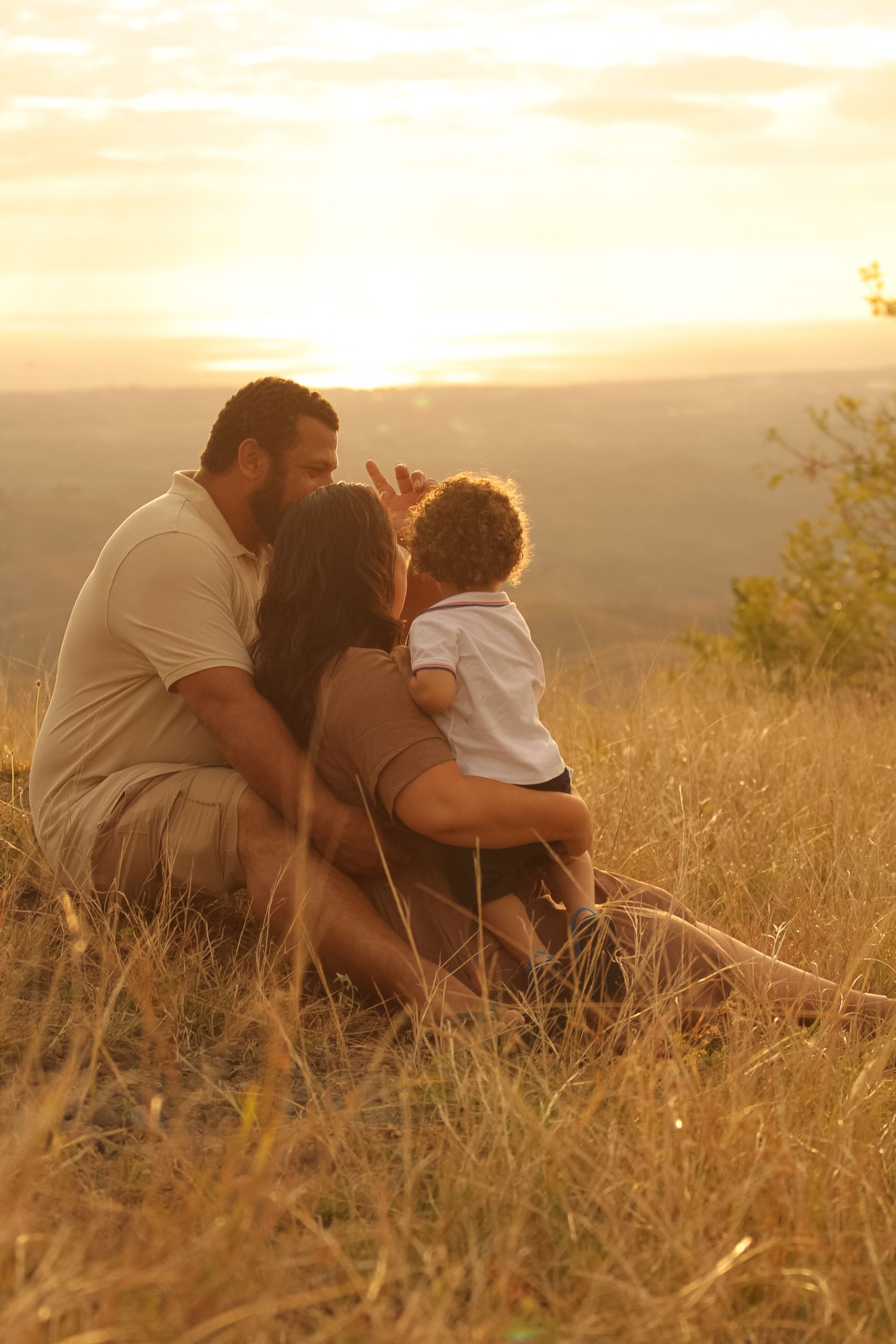 Family sits together watching sunset in golden field during magic hour.
