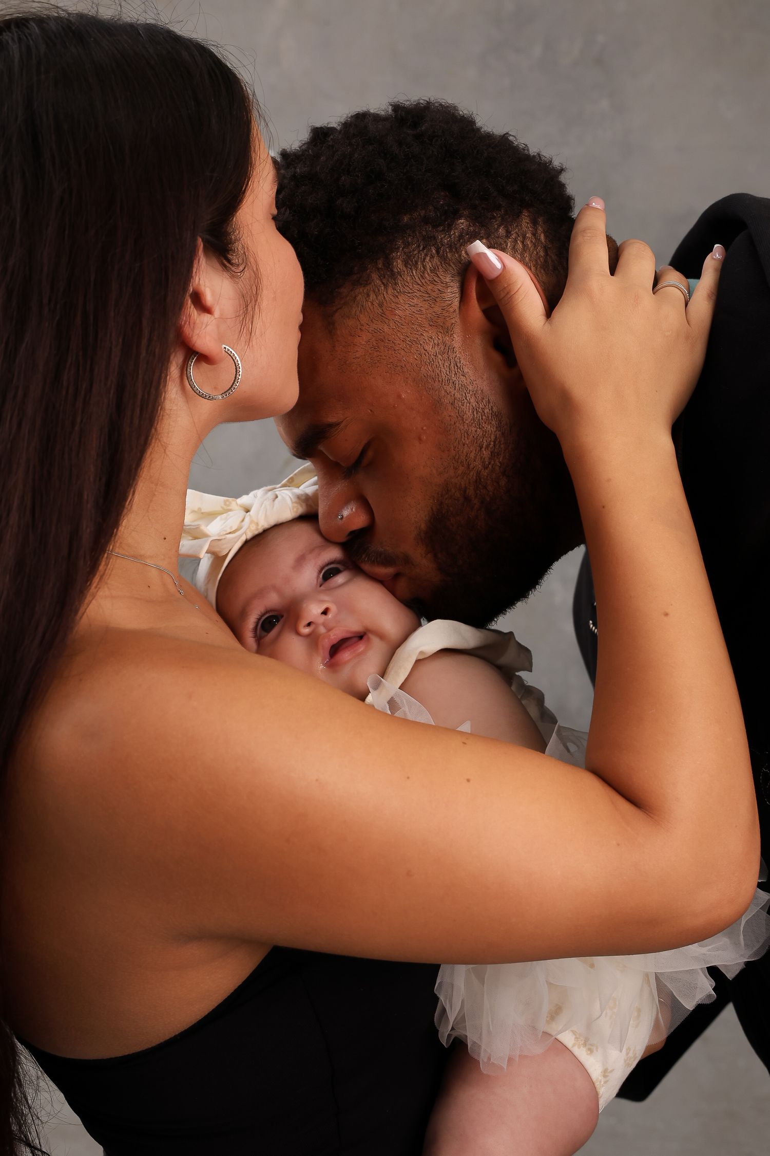 An intimate family moment captured as parents embrace their infant child.