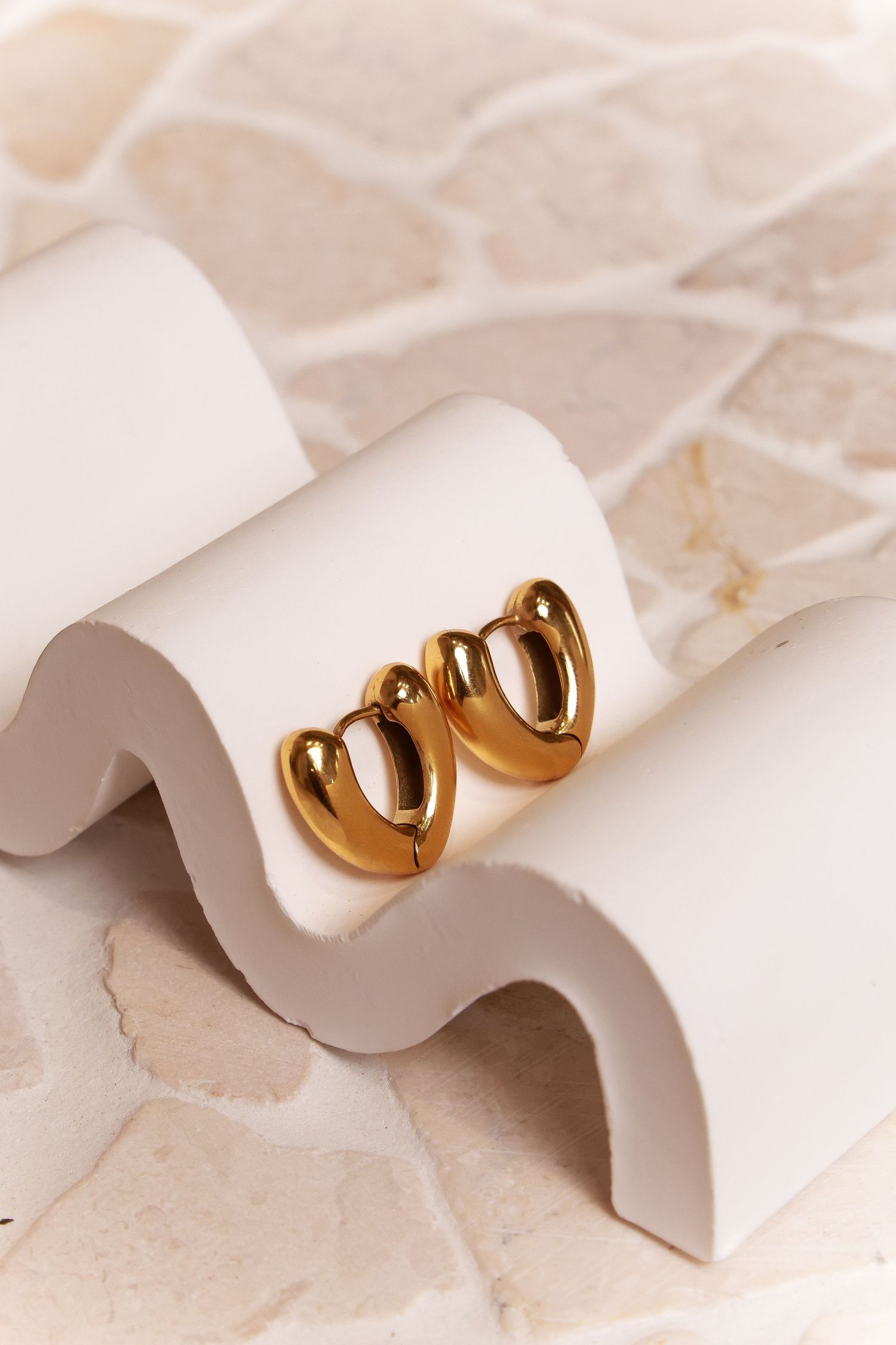 Gold heart-shaped hoop earrings displayed on white curved stand.