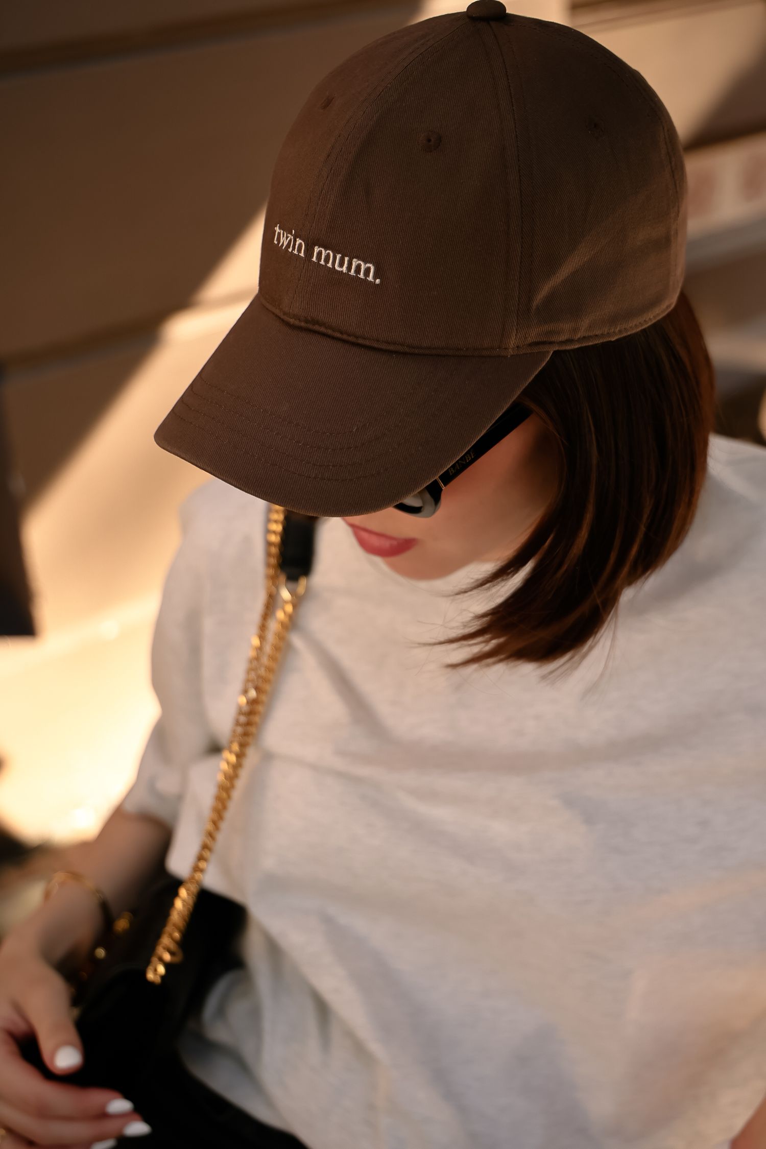 A person wearing a casual brown baseball cap with 'mum' text and a white t-shirt in warm lighting.
