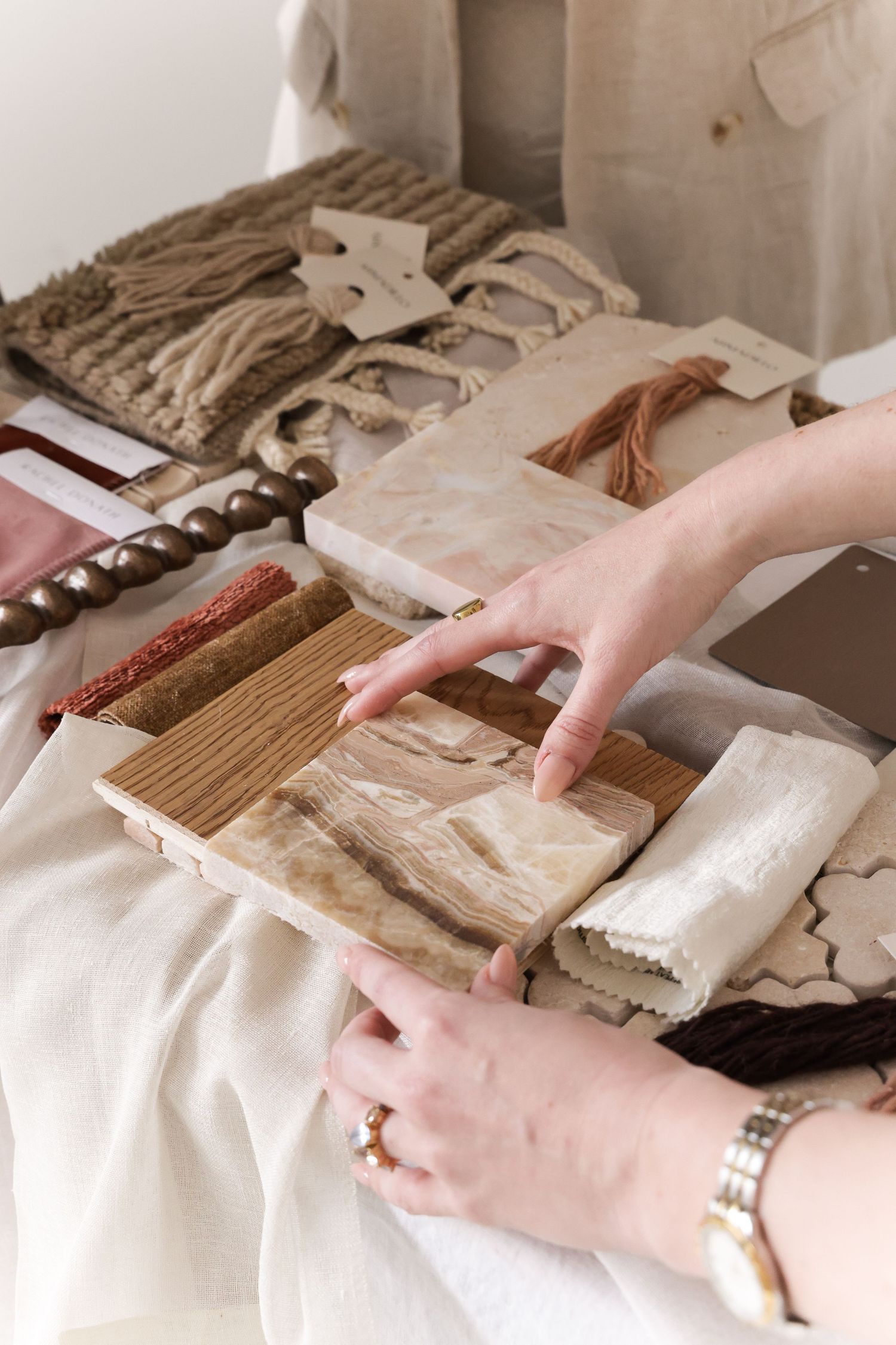 Hands arranging neutral-toned fabric swatches and material samples on white surface.