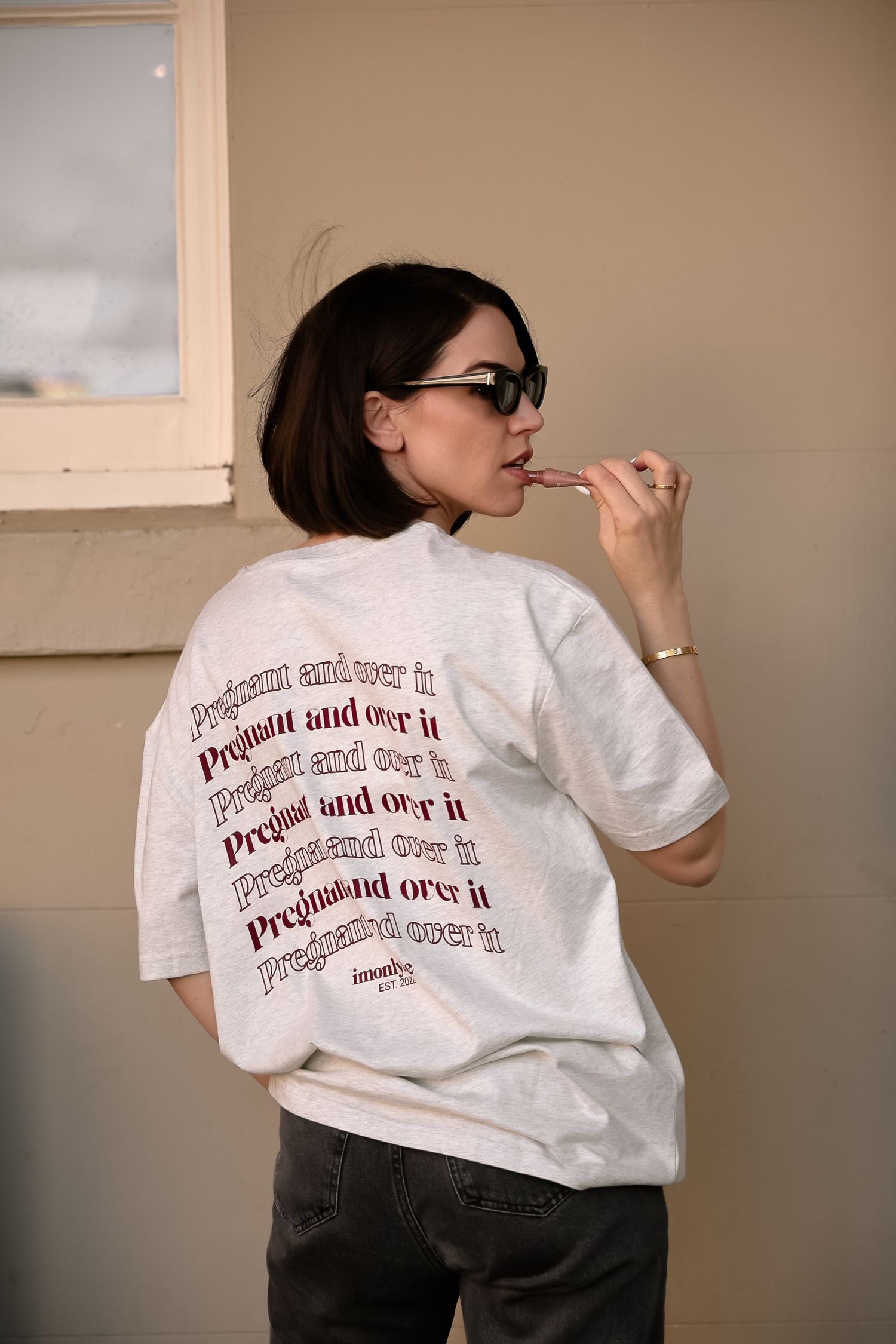 Back view of white sweatshirt with repeating red text design worn by person in glasses.