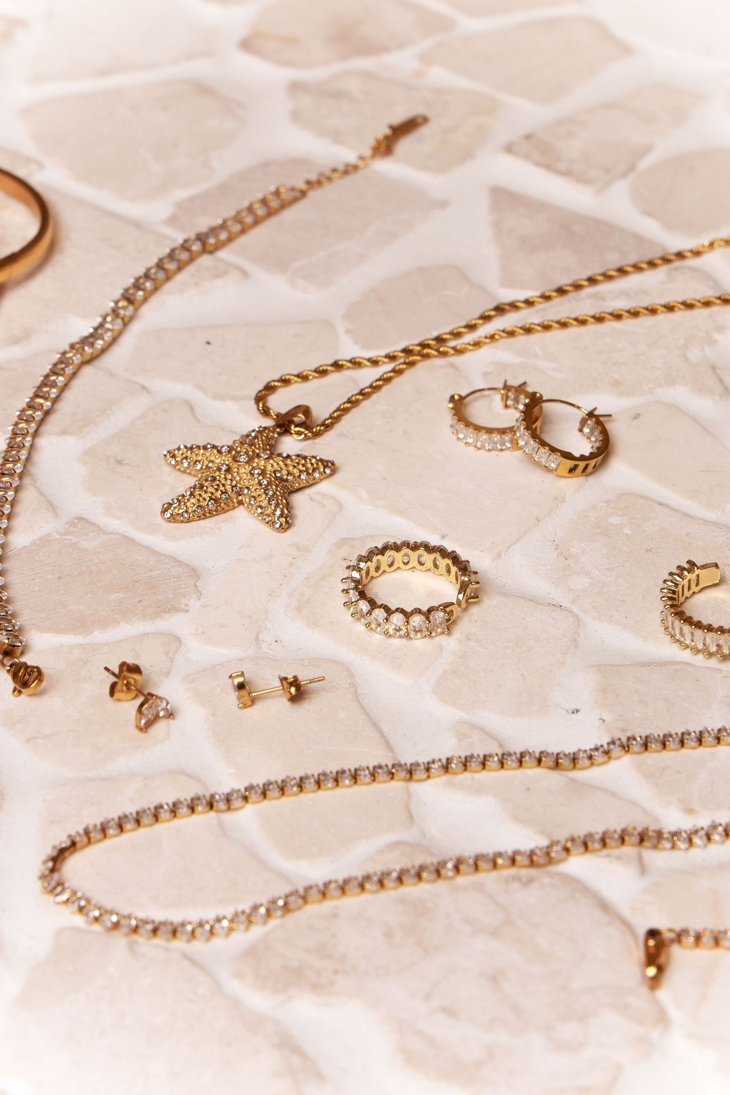 Flat lay of gold jewelry including starfish pendant and rings on textured surface.