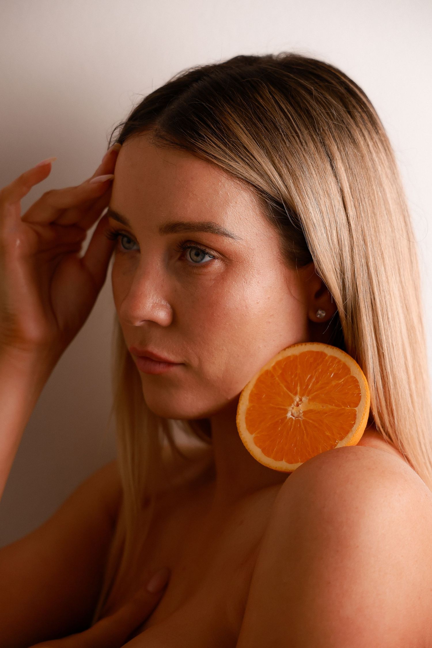 A creative beauty portrait holding orange slices against the face in warm lighting.