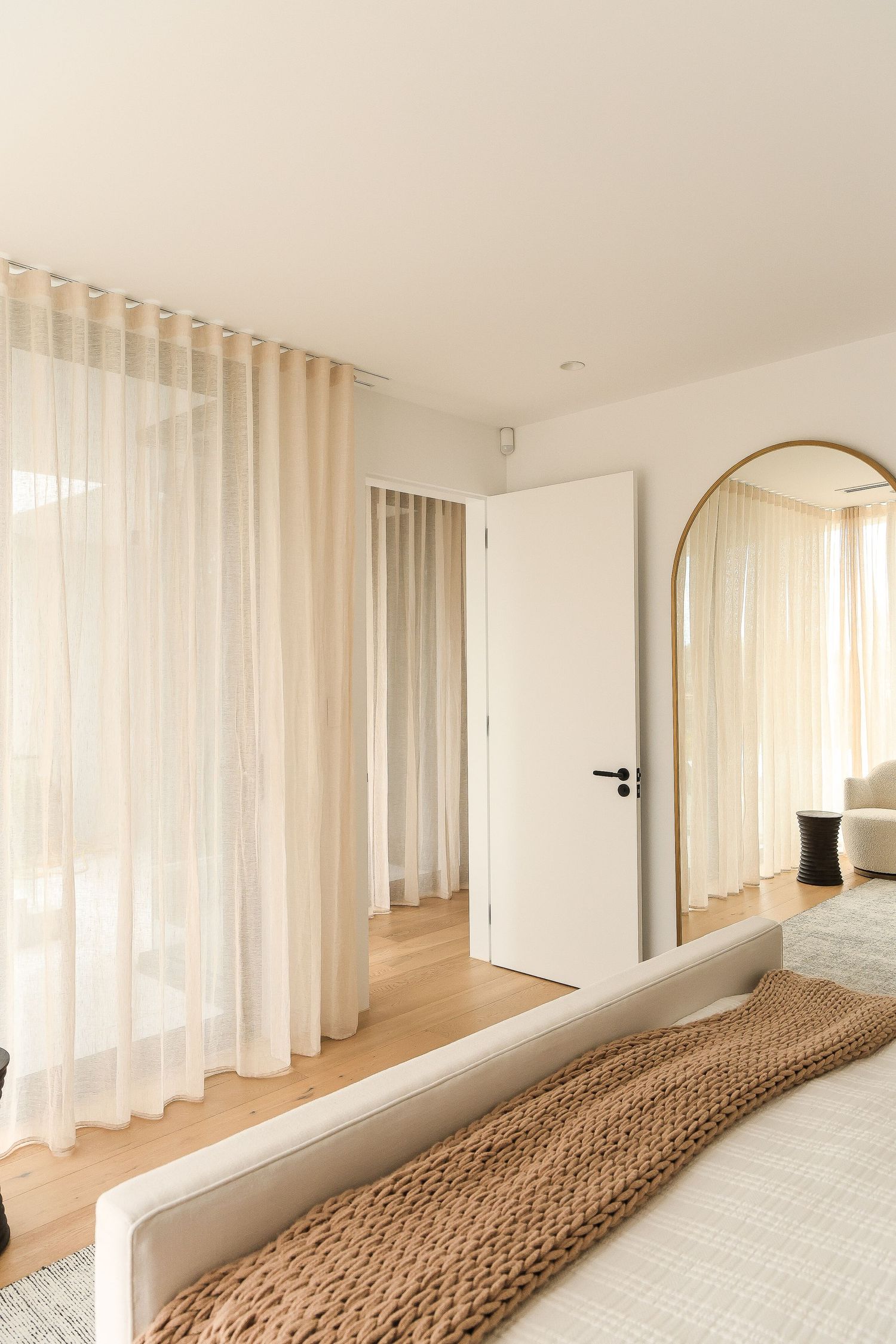 Bright bedroom interior with white bedding, sheer curtains, and natural wood flooring.