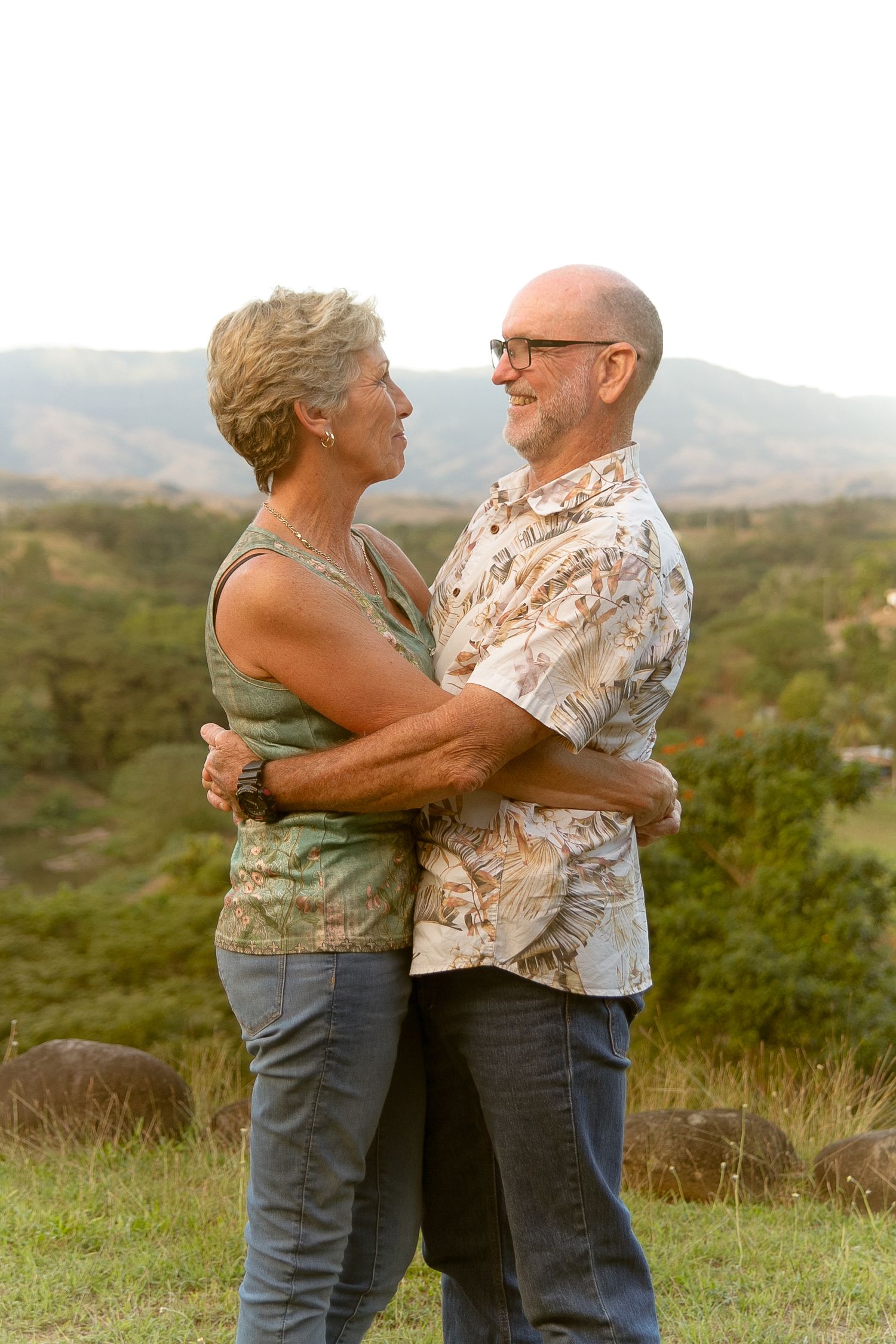 Couple embraces while standing on grassy hilltop during sunset.