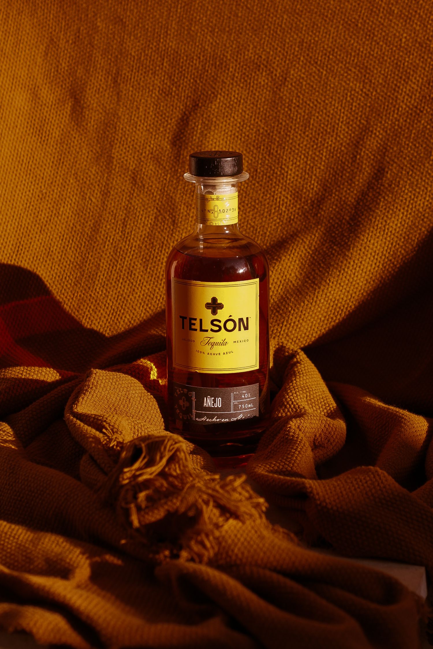 Telson spirits bottle styled on draped fabric with dramatic amber lighting.
