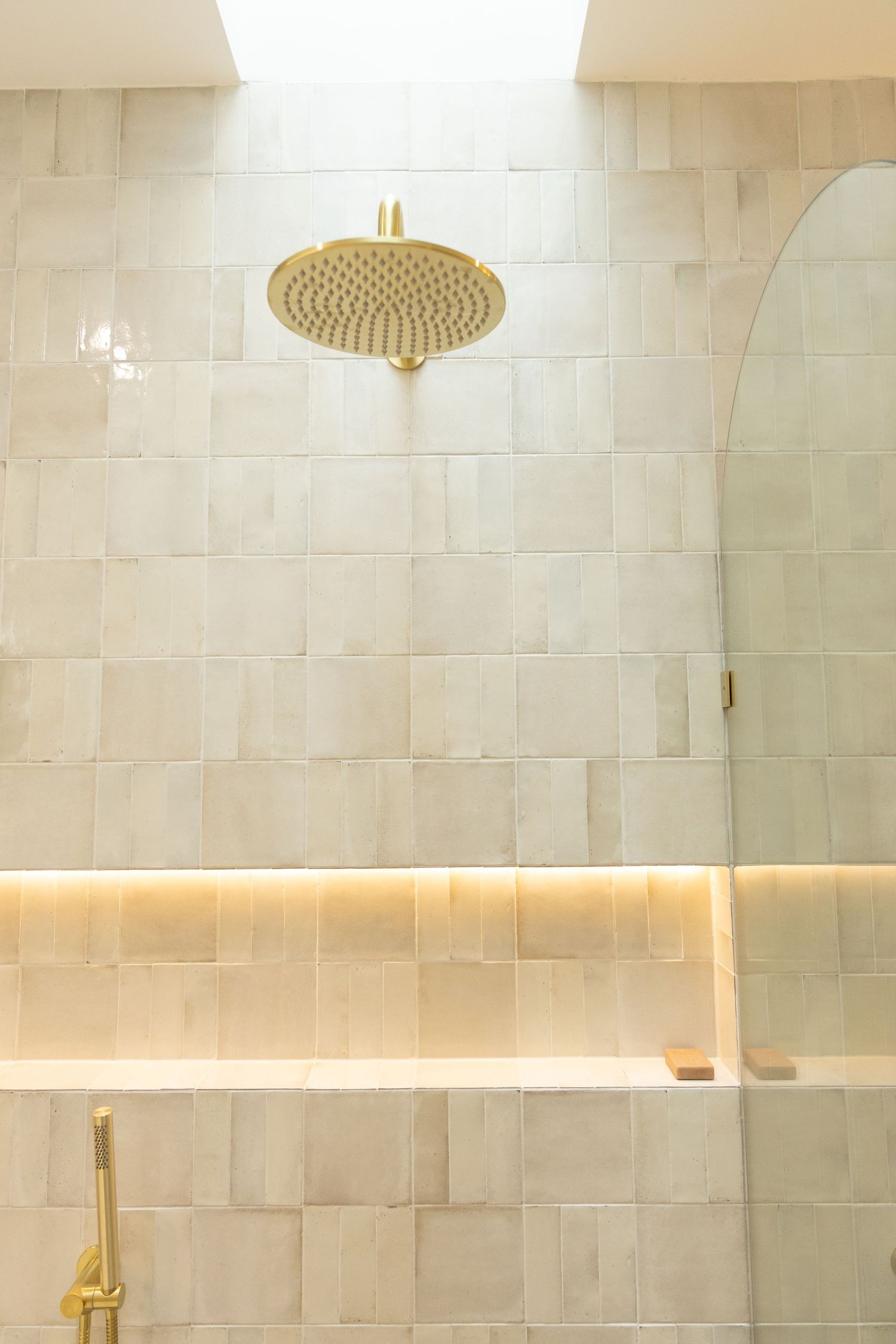 Luxurious shower space with cream-colored tile walls and gold rainfall showerhead.