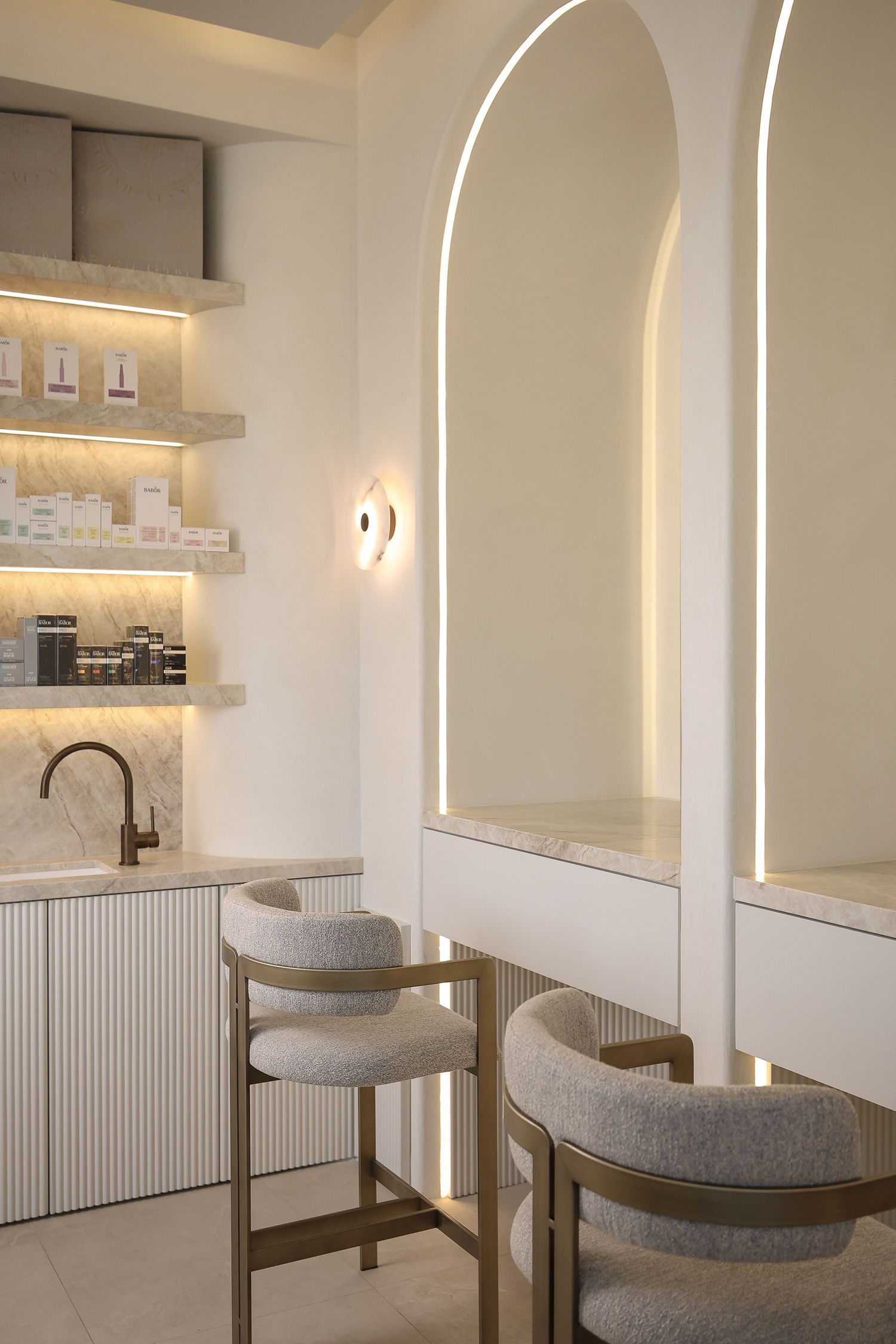 Elegant dining area with arched lighting features, gray upholstered seating, and white walls.